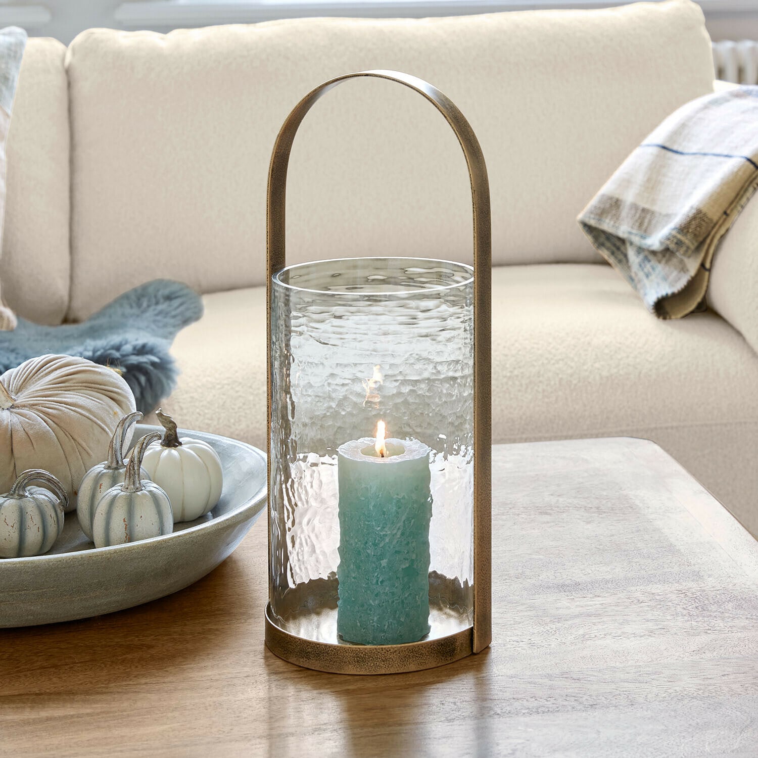 Portavelas Omirah Linterna de cristal con asa de latón y vela azul sobre mesa de madera en salón