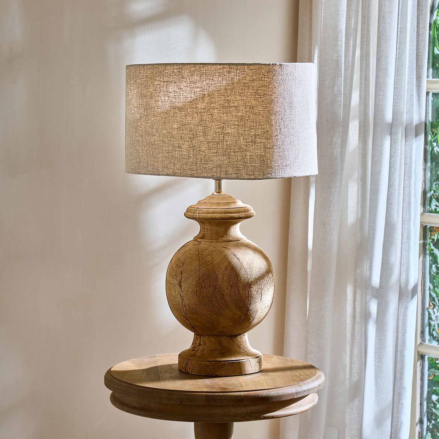 Lámpara de mesa con base de madera y pantalla beige sobre mesa redonda junto a ventana