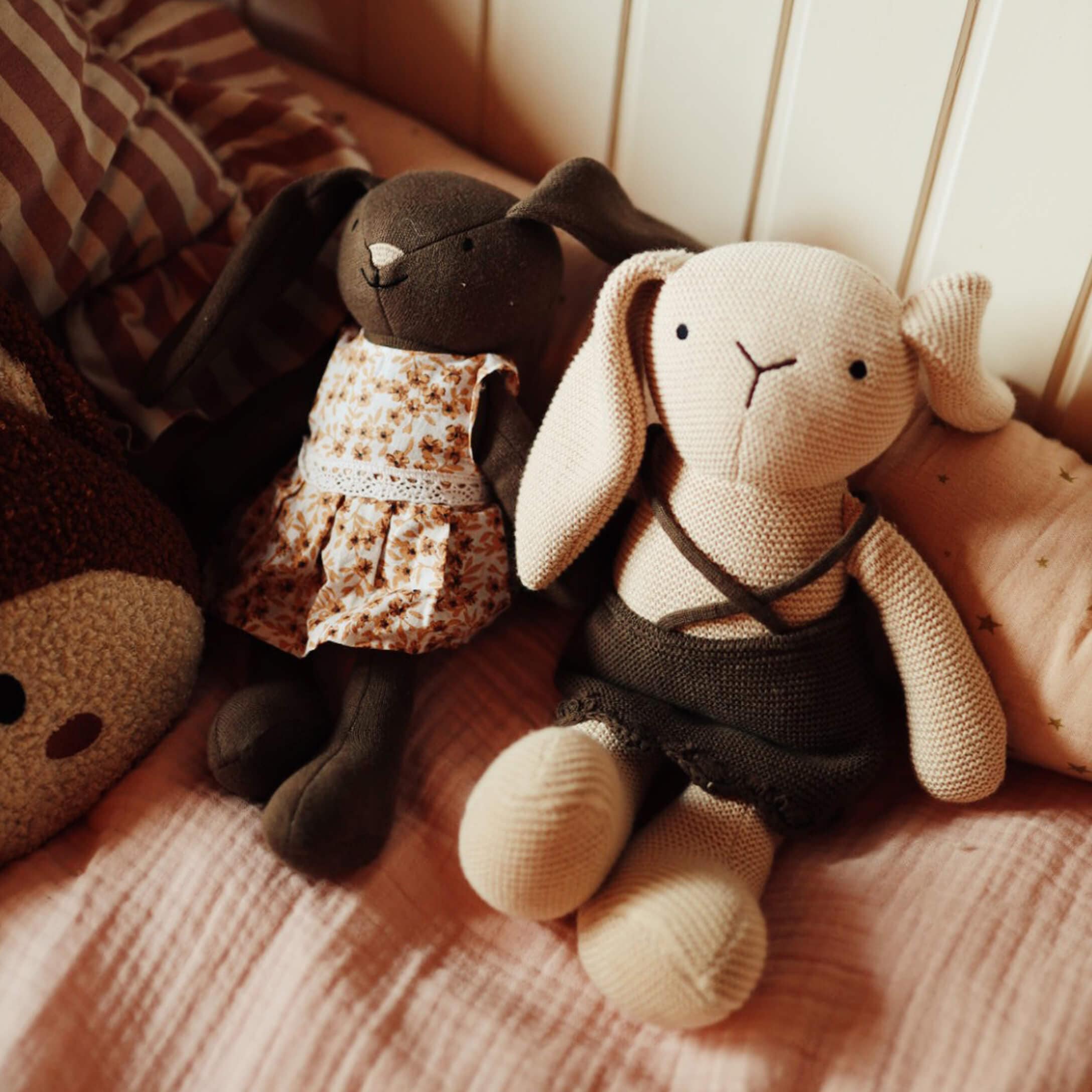Dos conejos de peluche con vestidos sobre ropa de cama rosa, juguetes suaves para niños