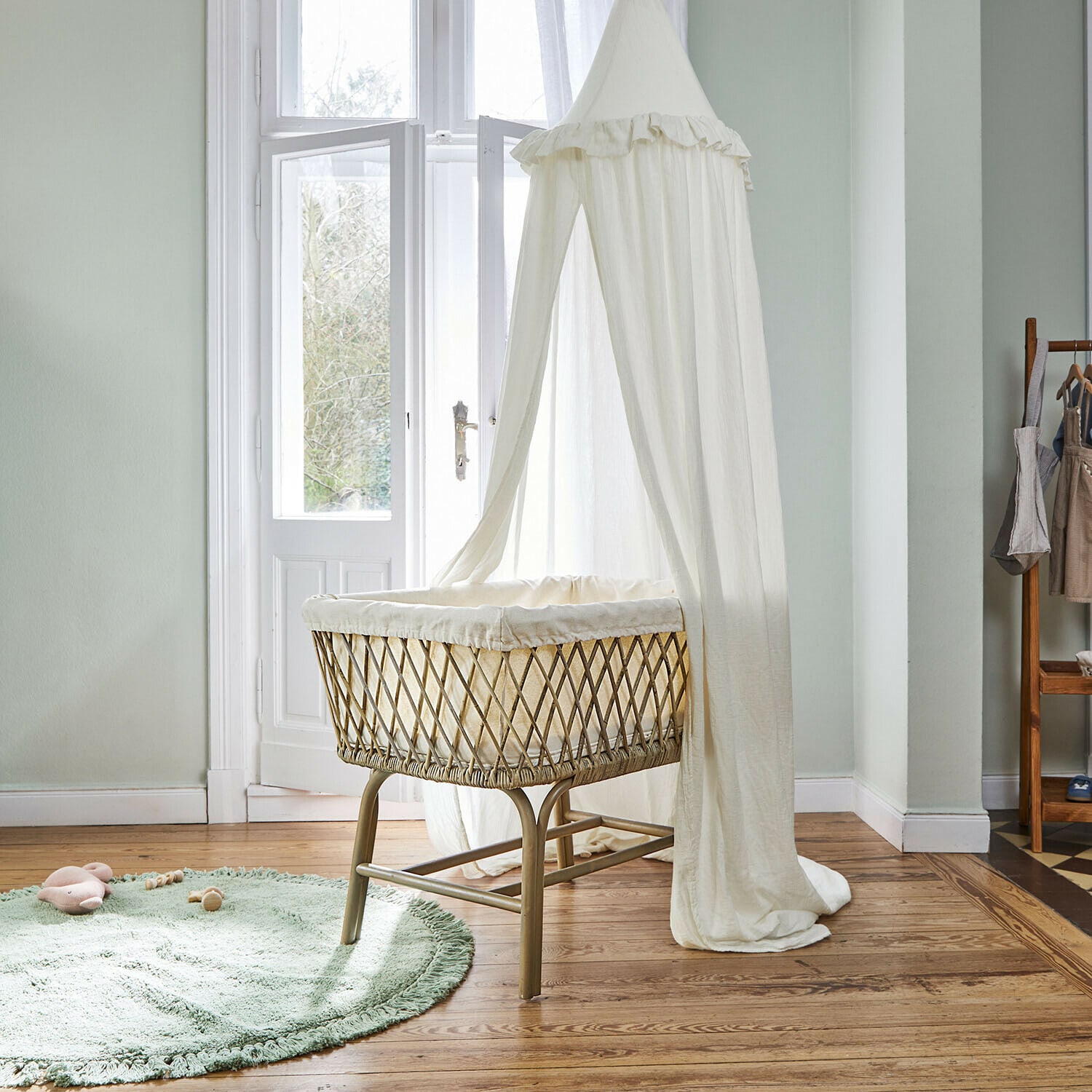 Cuna de ratán natural con dosel blanco ligero en habitación infantil luminosa