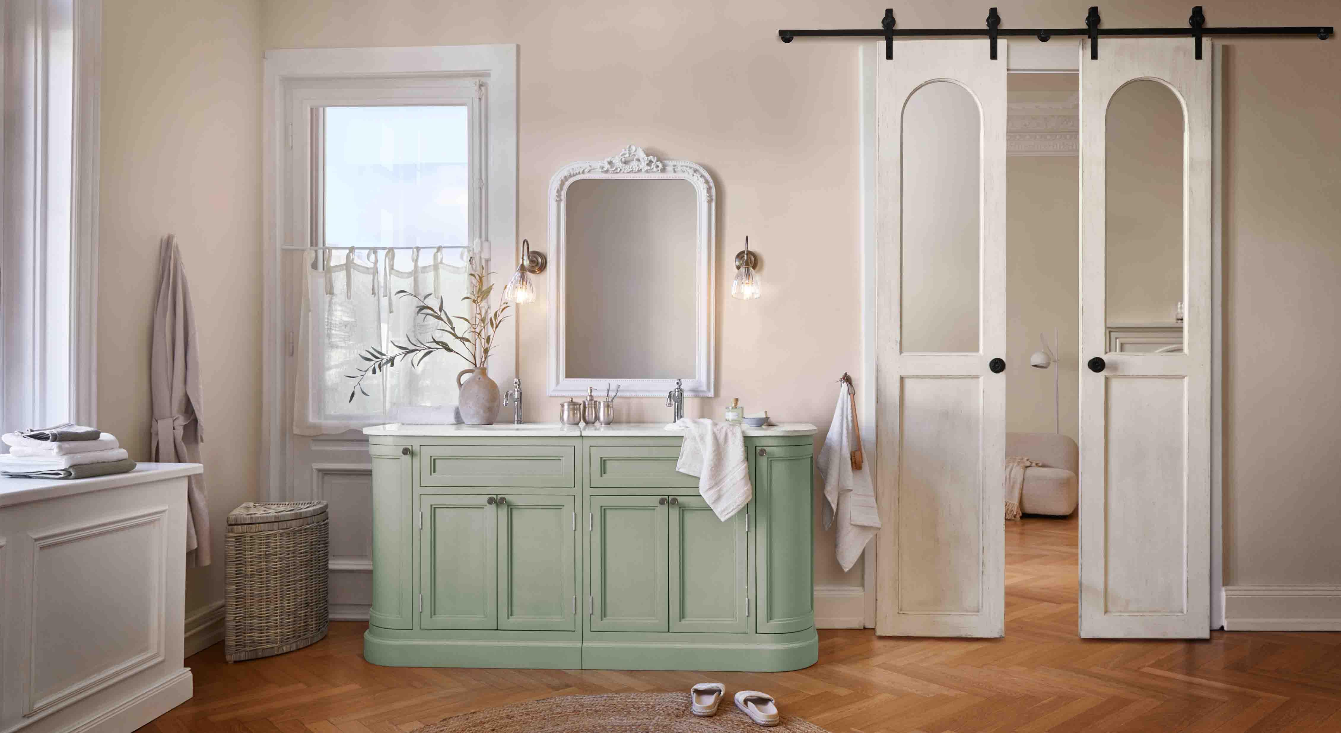 Mueble de baño verde con encimera blanca y espejo vintage decorativo en marco tallado