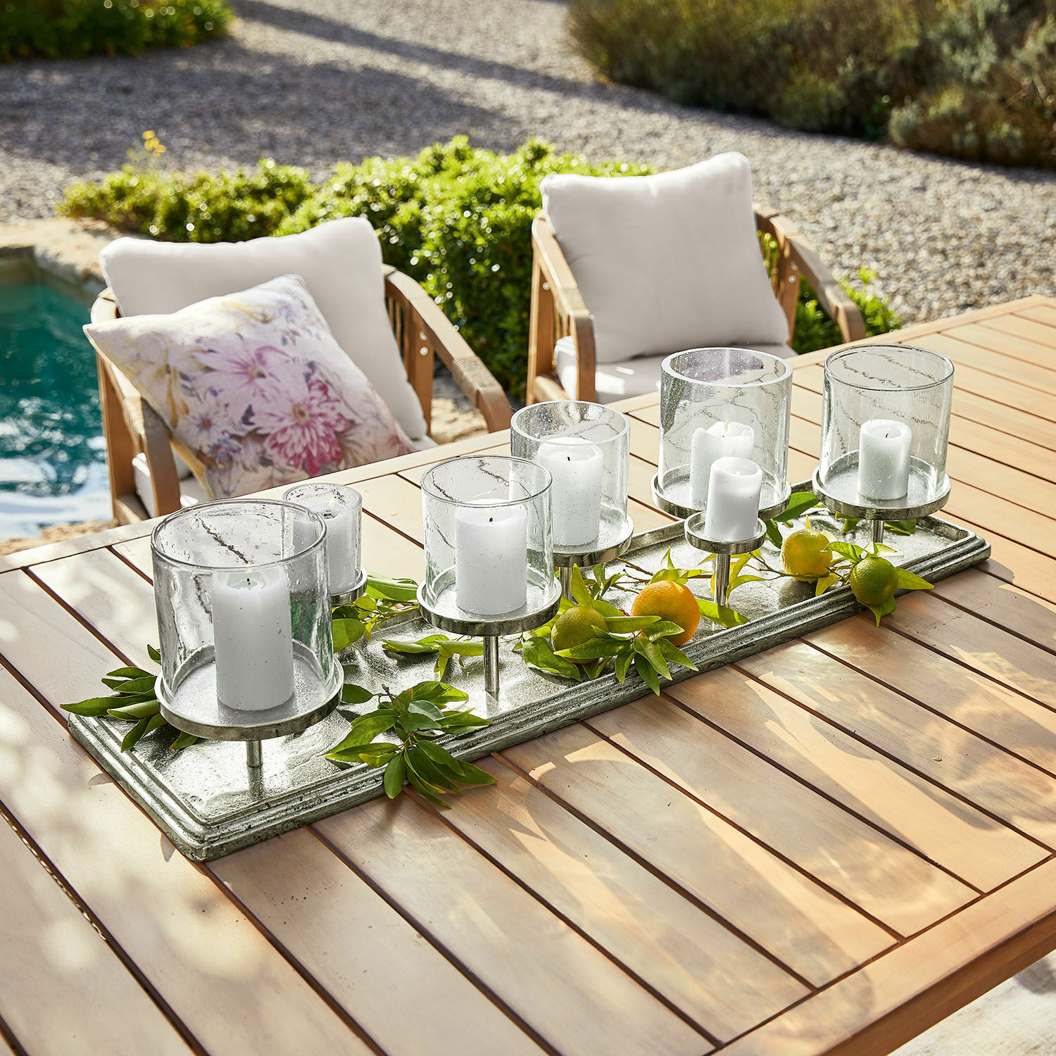 Bandeja para velas Devonne Candelabro decorativo de vidrio y metal con velas blancas sobre mesa de madera en jardín