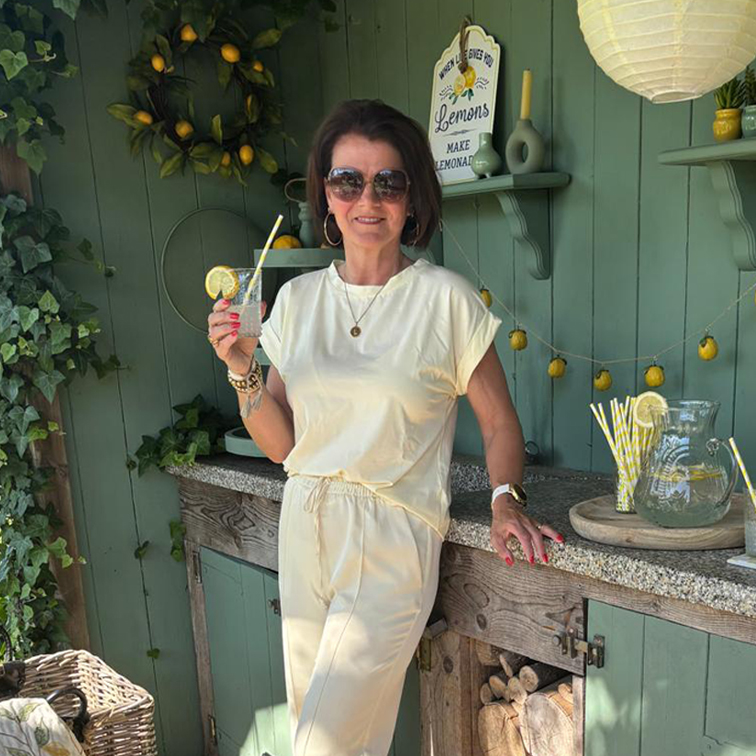 Mujer con conjunto crema disfruta de limonada frente a pared verde con decoración de limones