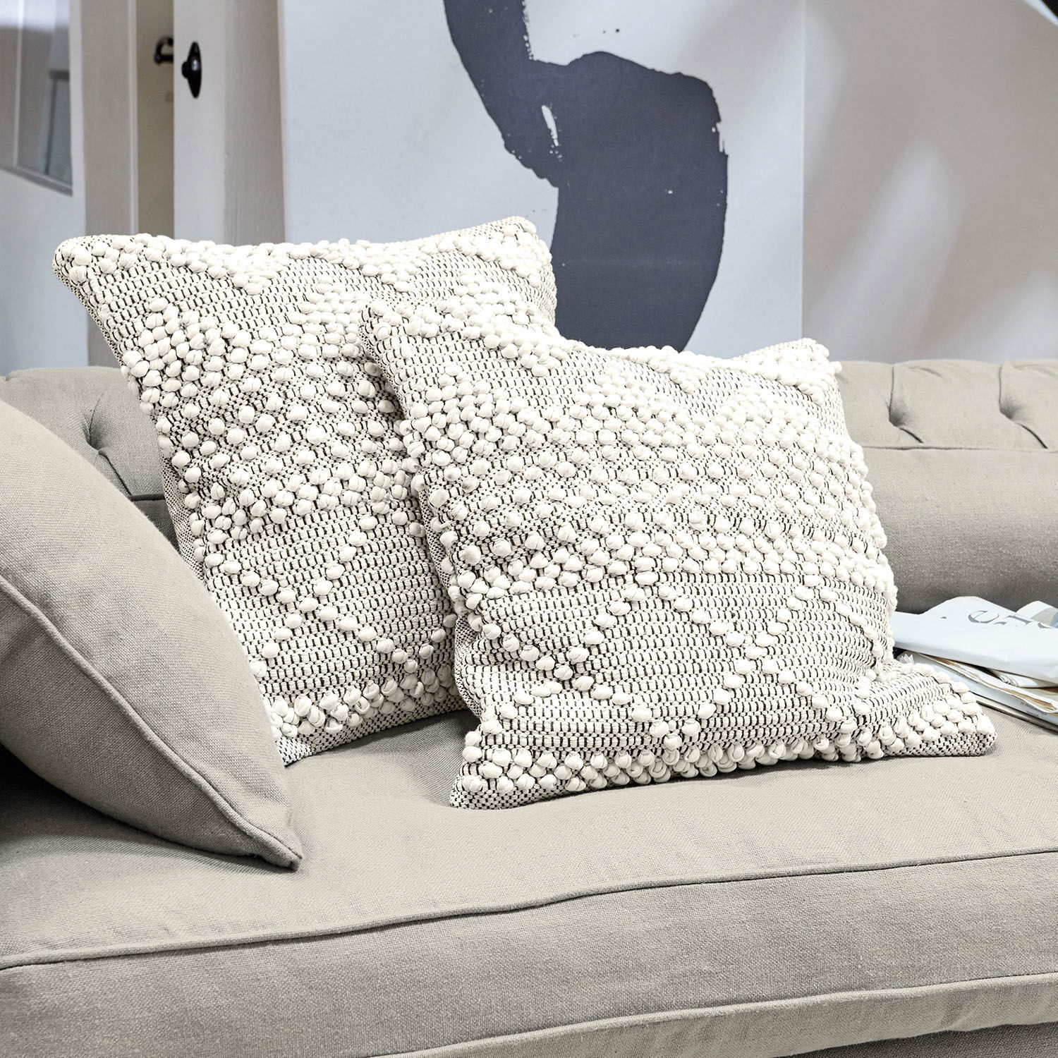 Dos cojines decorativos crema de algodón con textura y patrón geométrico sobre sofá gris