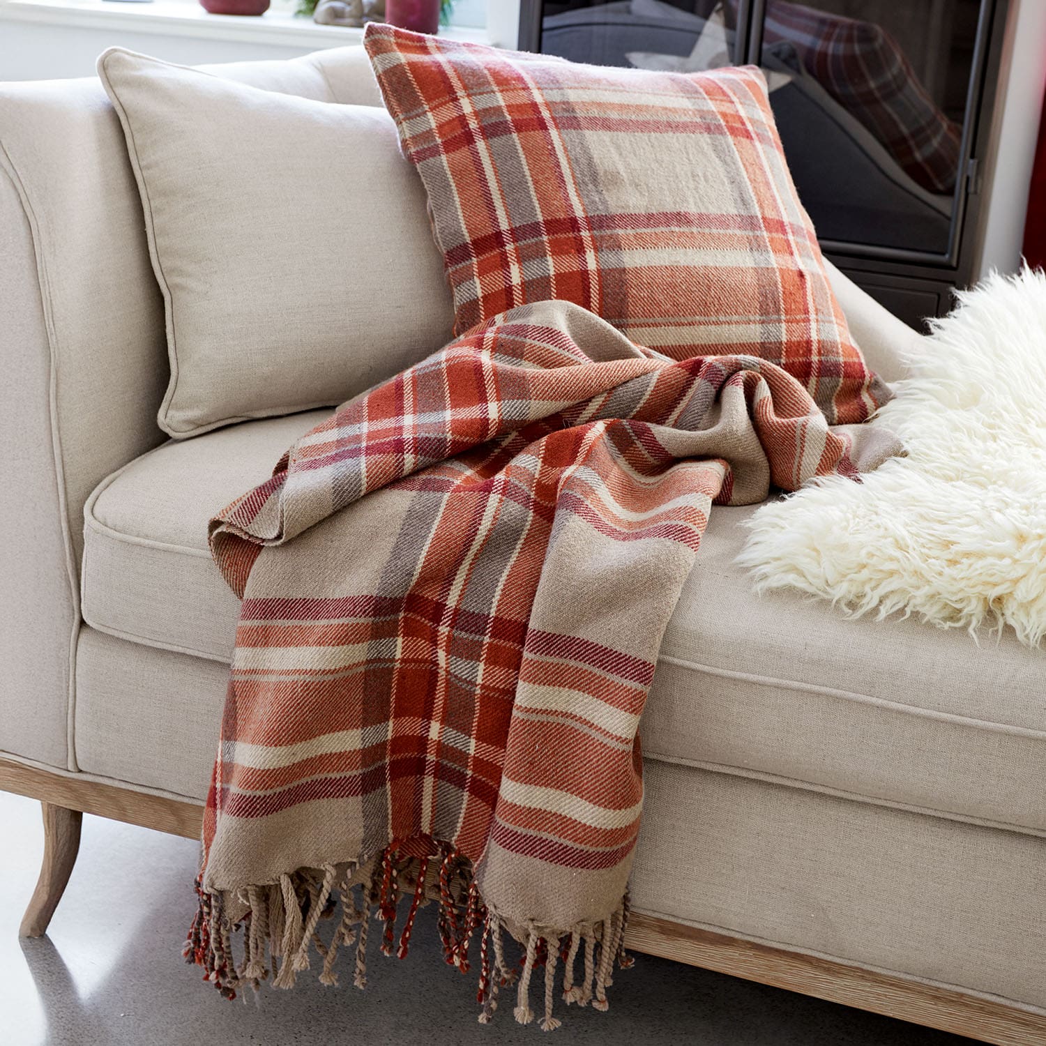 Sofá beige con cojín y manta de cuadros en tonos rojos y marrones para salón acogedor