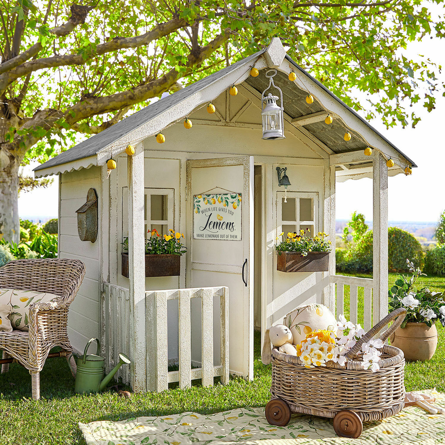 Casa infantil Pouponnet Casita de jardín de madera blanca con decoraciones de limón y cesta de mimbre con ruedas sobre césped