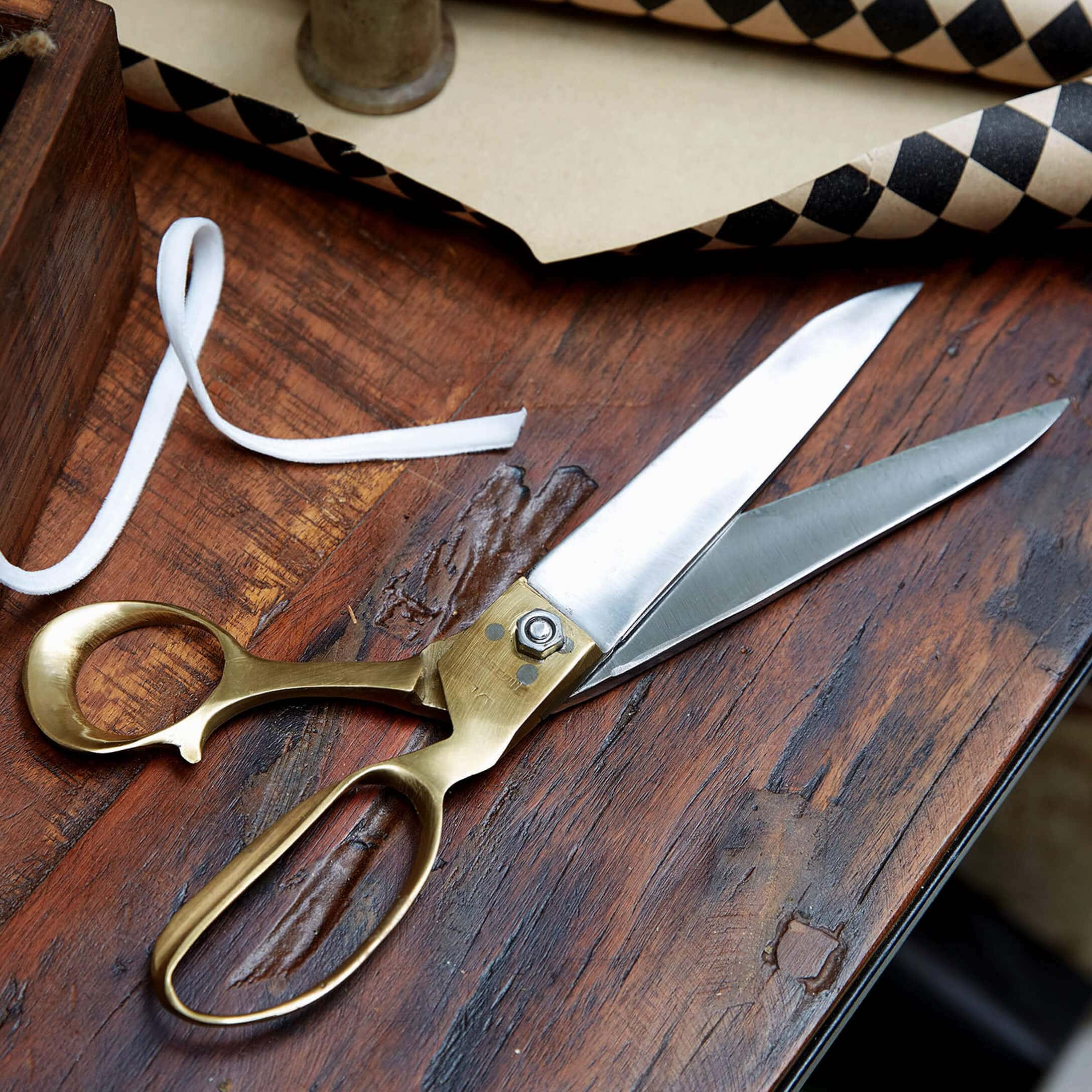 Tijeras de costura de acero inoxidable y latón sobre mesa de madera para telas y costura