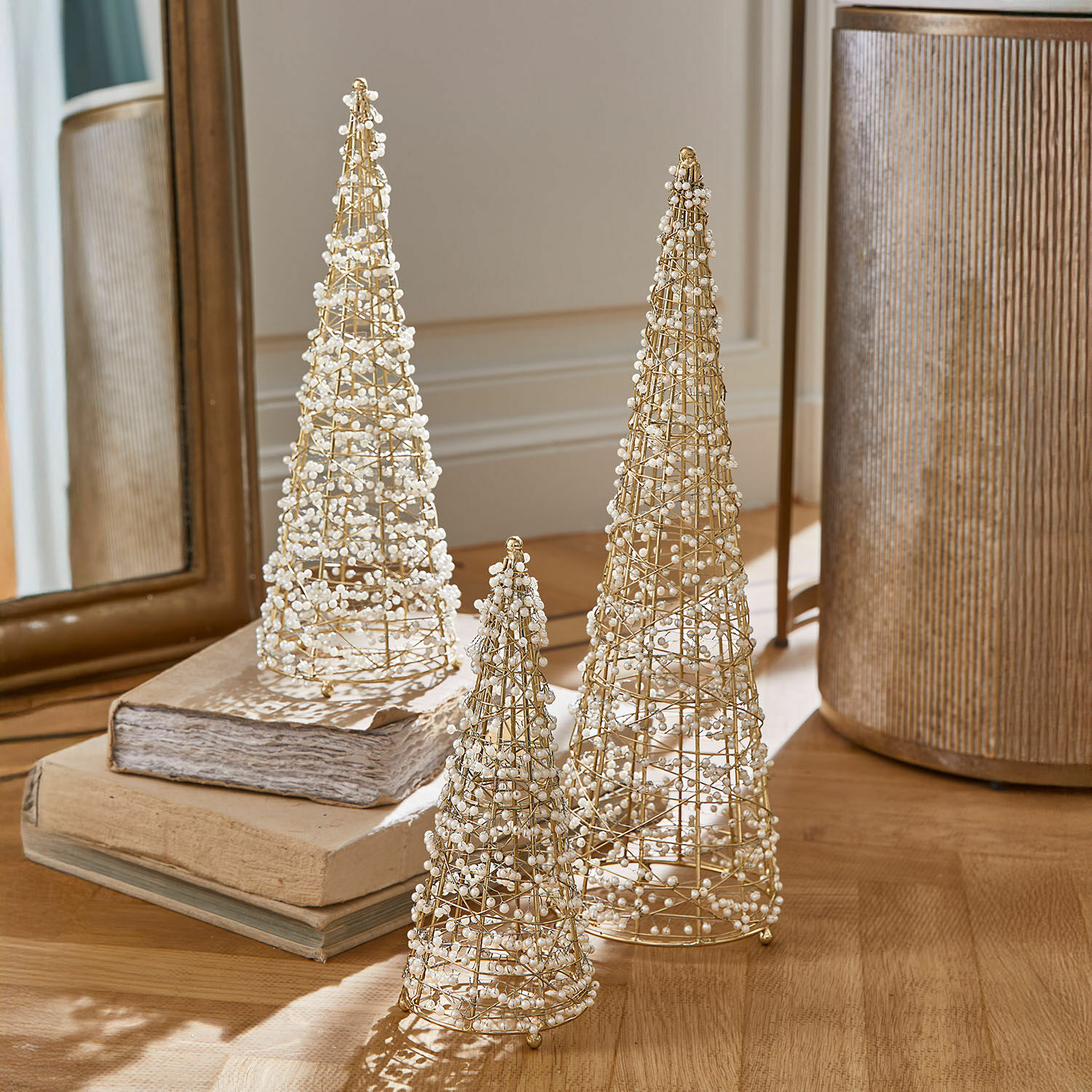 Set de 3 árboles decorativos Amelioro Conjunto de tres conos decorativos de alambre dorado con perlas blancas sobre mesa de madera