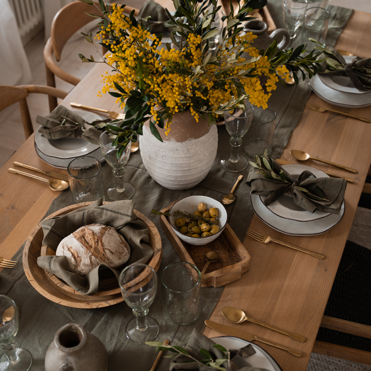 Mesa rústica de madera con vajilla blanca, cuencos de madera y flores amarillas en jarrón de barro
