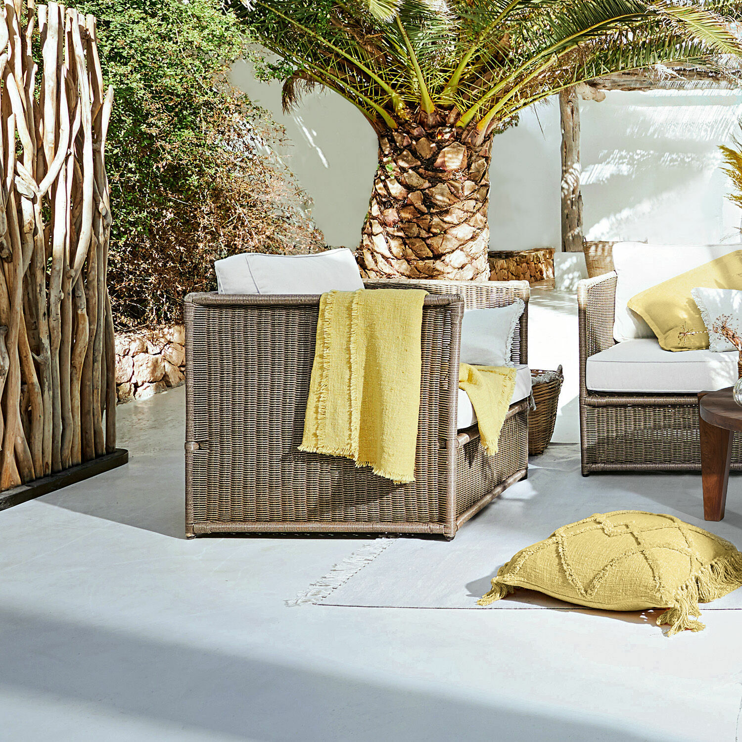 Sillón Lesmont Conjunto de muebles de jardín de ratán marrón con cojines blancos y detalles amarillos en terraza soleada