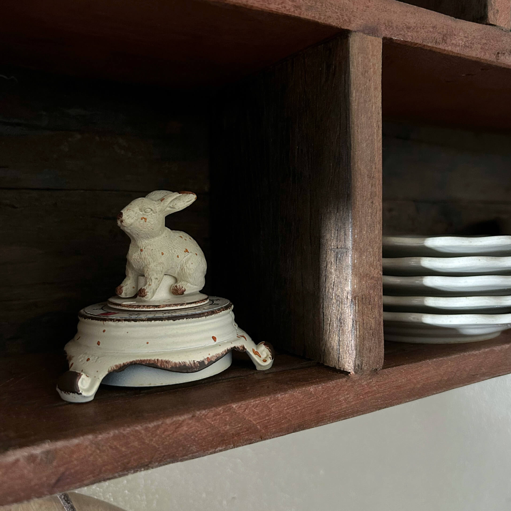 Recipiente de cerámica blanca con tapa de conejo en estante de madera junto a platos