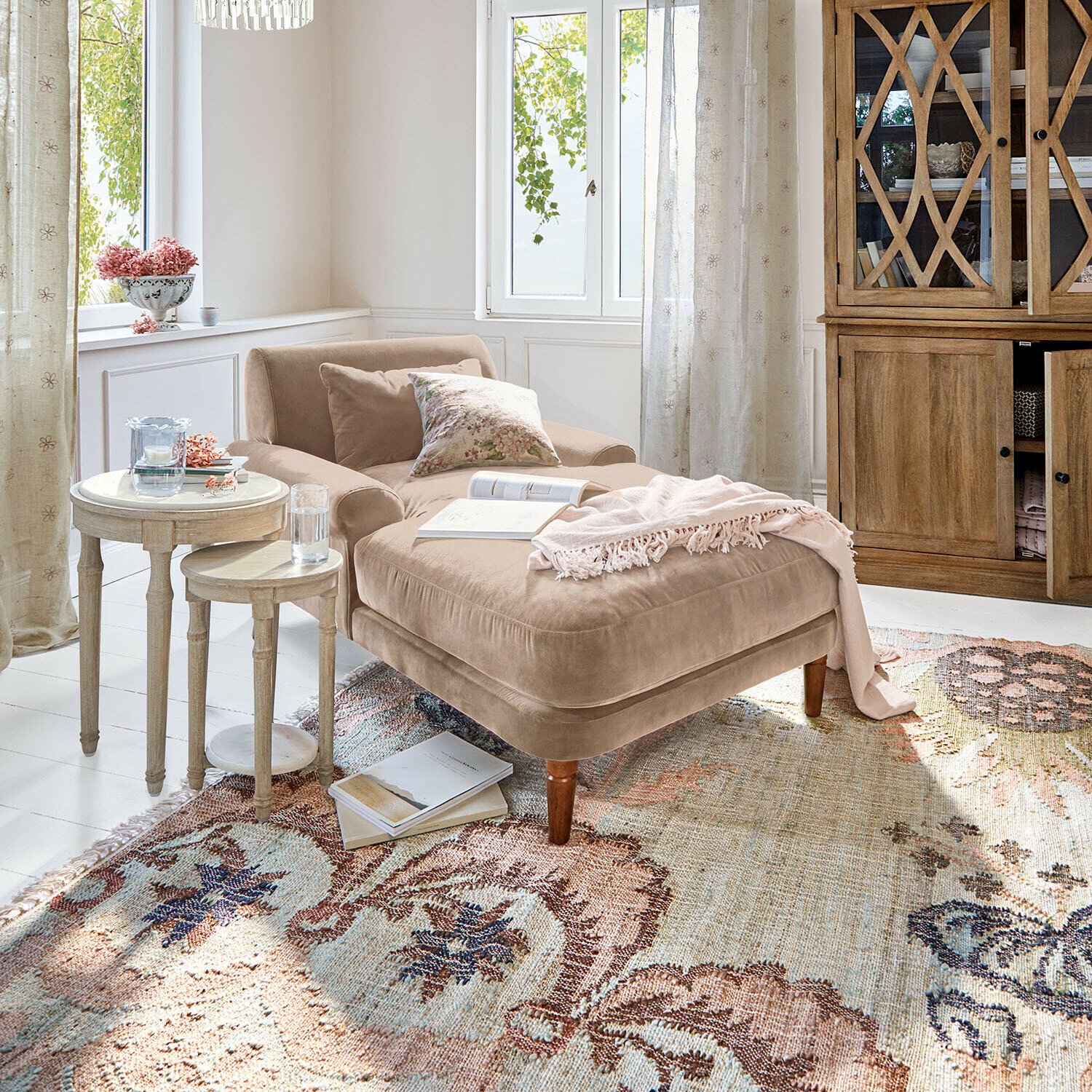 Chaise longue Jouvrelle Chaise longue beige de terciopelo con cojines y manta rosa sobre alfombra estampada en salón luminoso