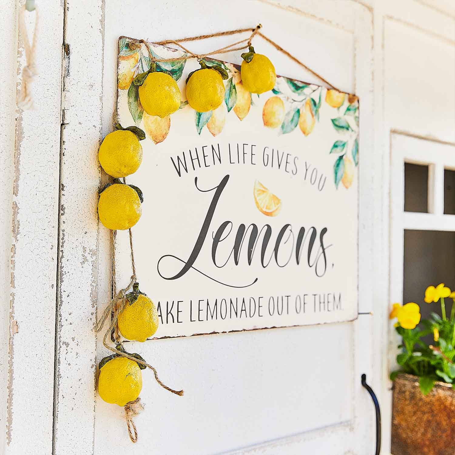 Cartel decorativo con diseño de limones y guirnalda de limones amarillos colgada en puerta blanca