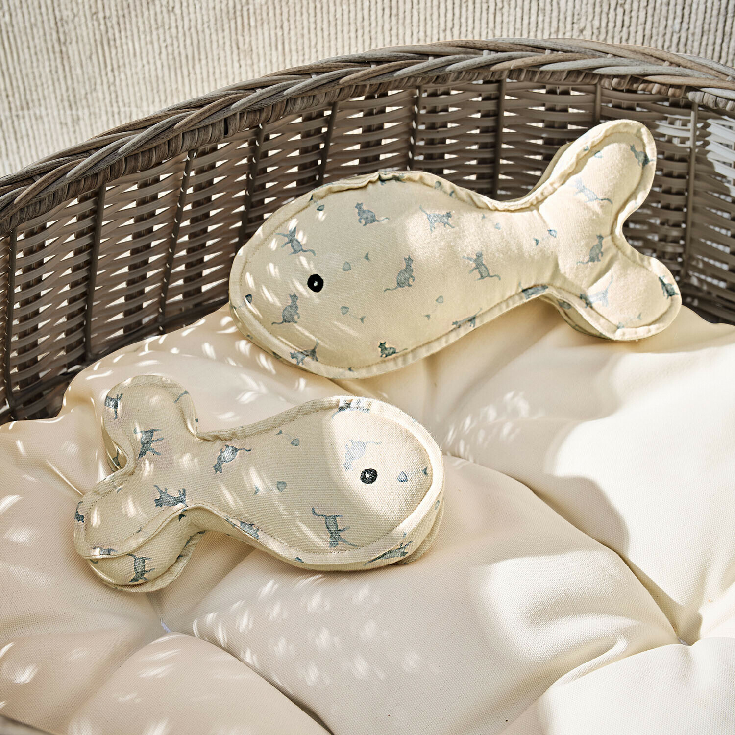 Cojines beige con forma de pez y estampado de gatos sobre sillón de mimbre con cojín claro