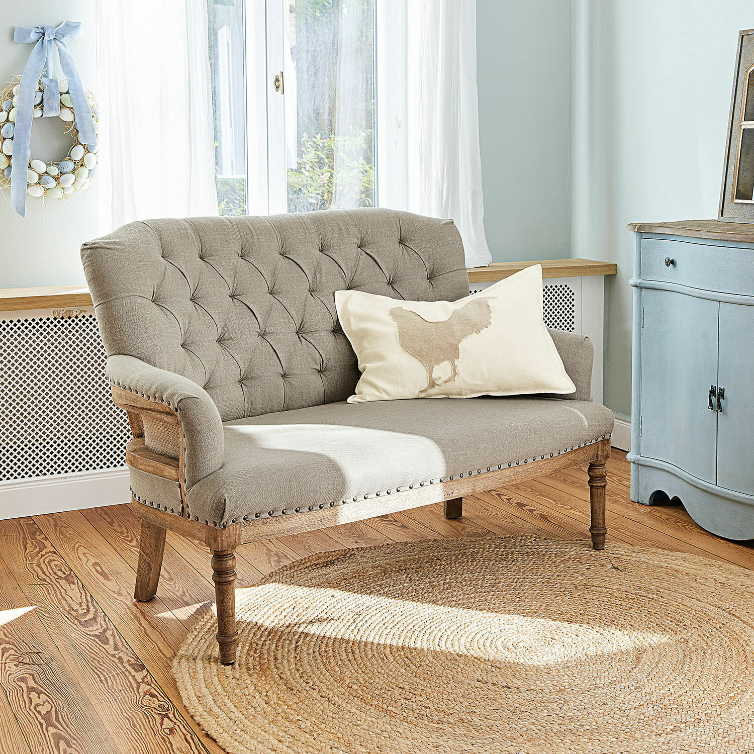 Sofá Kingsley Sofá beige tapizado con marco de madera y botones decorativos en sala luminosa