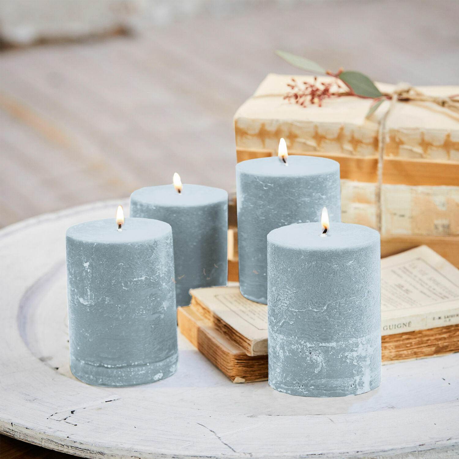 Conjunto de cuatro velas azules de cera sobre mesa blanca de madera con libros y regalo
