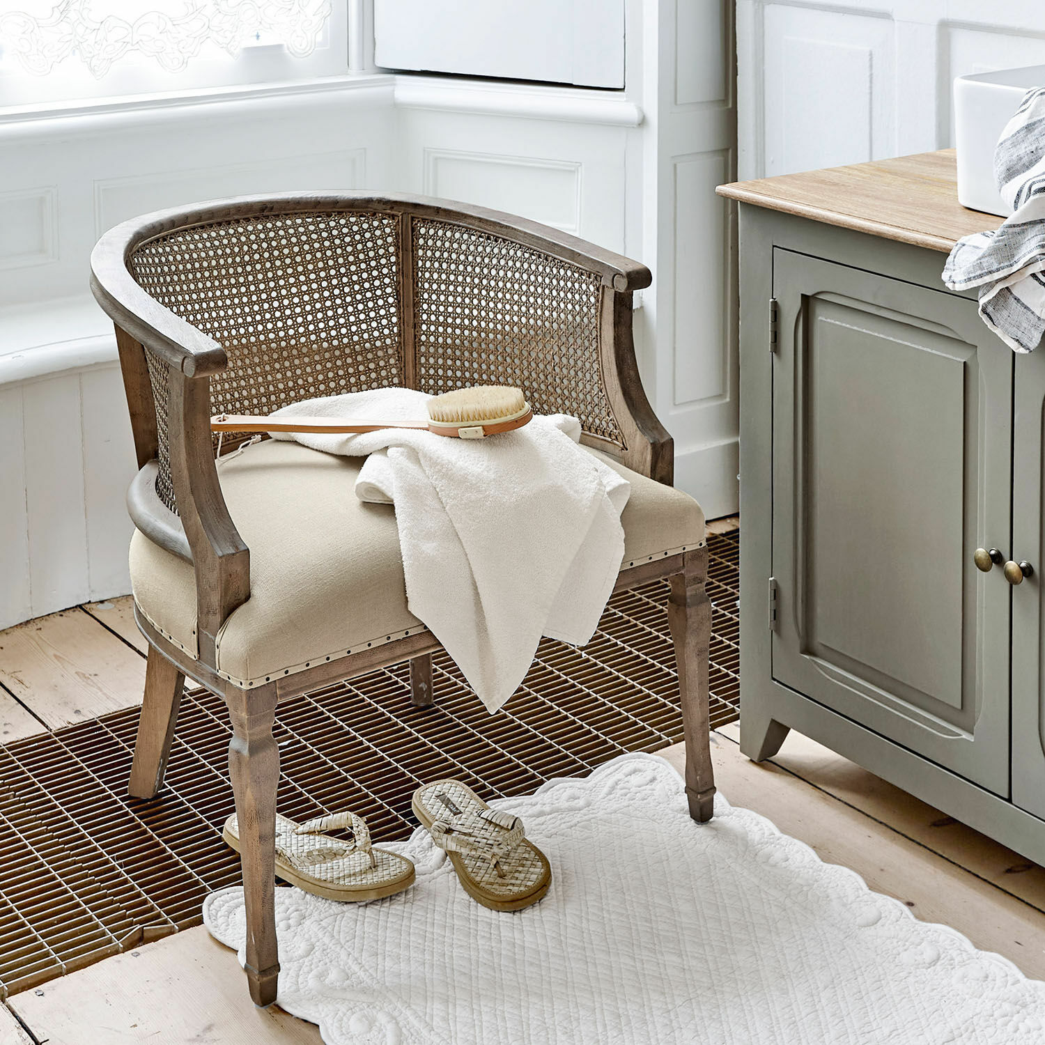 Silla Curbigny Silla de madera y ratán beige con asiento acolchado y toalla blanca en baño luminoso
