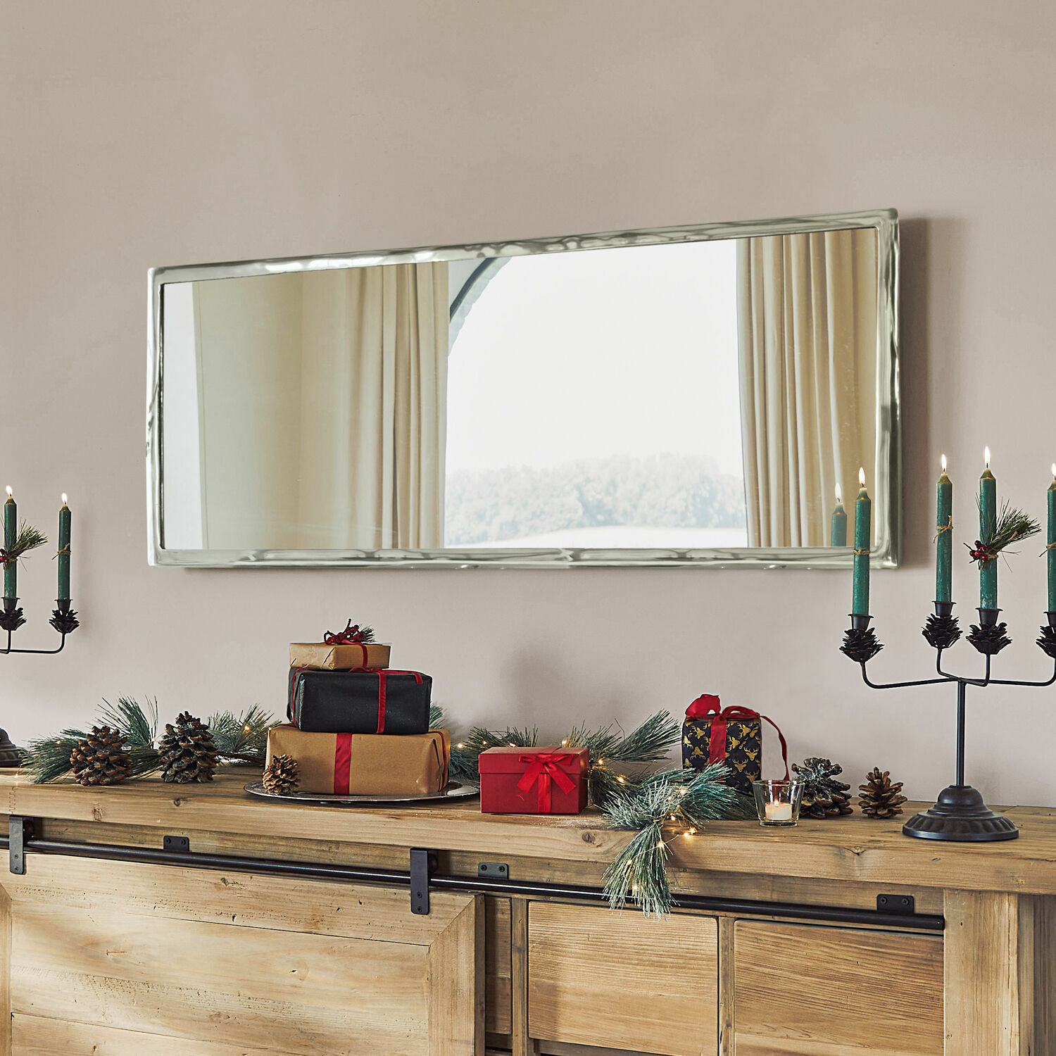 Espejo rectangular con marco metálico plateado sobre cómoda de madera con decoración navideña