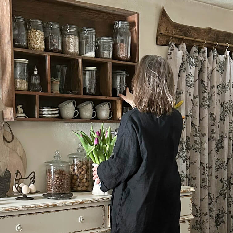 Mujer con vestido negro coge un tarro en estantería de madera en cocina rústica con ramo de tulipanes