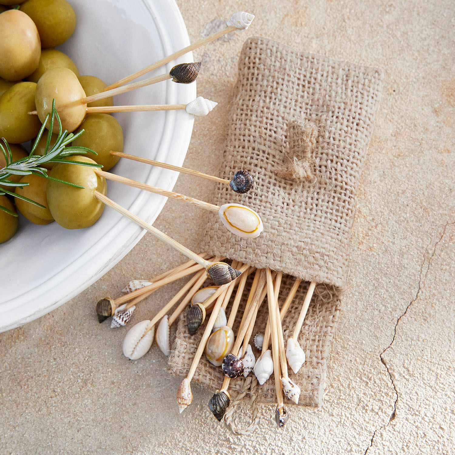 Juego de palillos con conchas naturales en bolsa de lino junto a aceitunas verdes