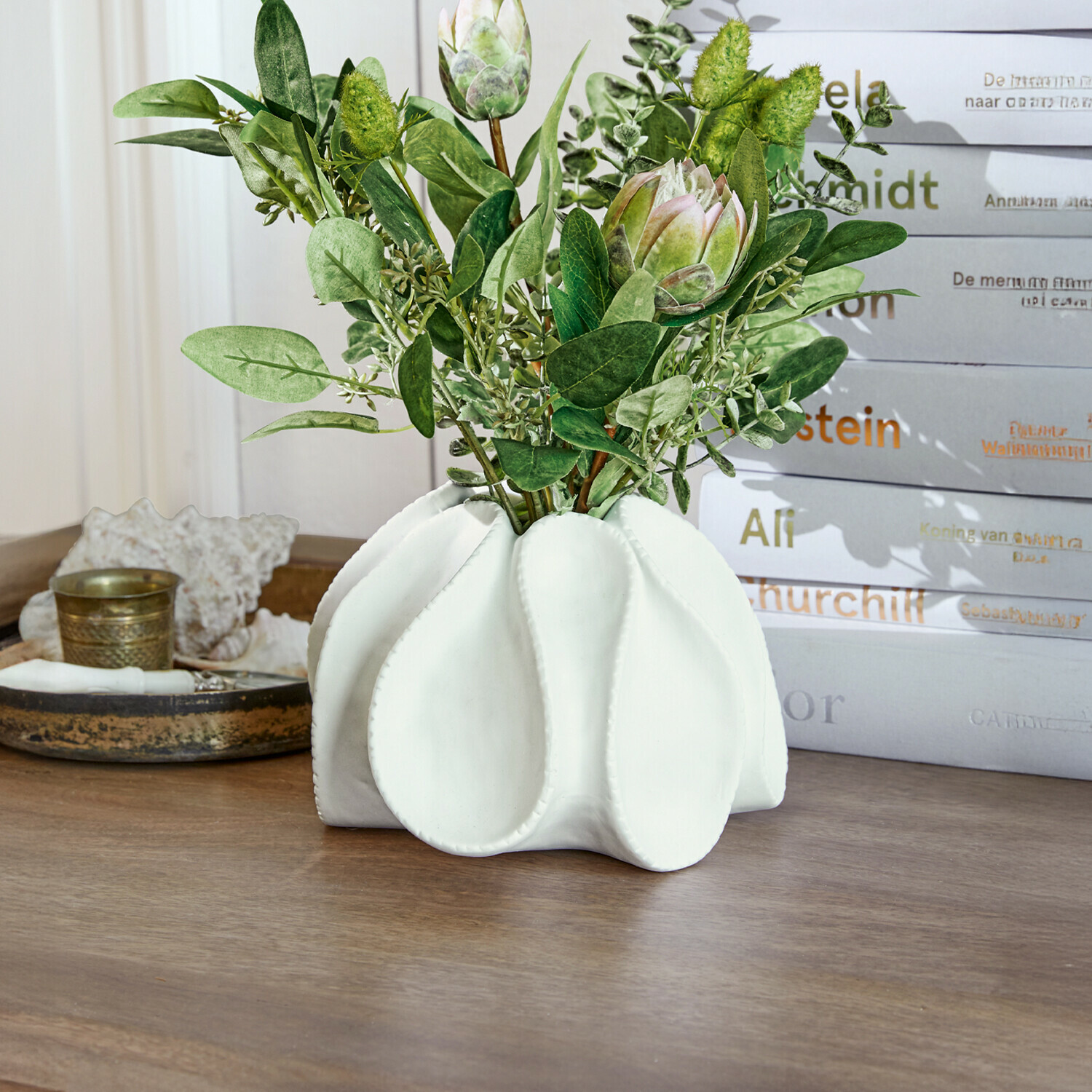 Jarrón de cerámica blanca con hojas verdes y flores decorativas sobre mesa de madera