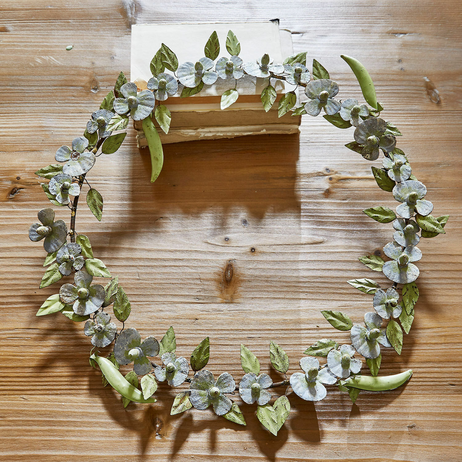 Corona Cecilia Corona decorativa de metal con hojas verdes y flores blancas sobre mesa de madera