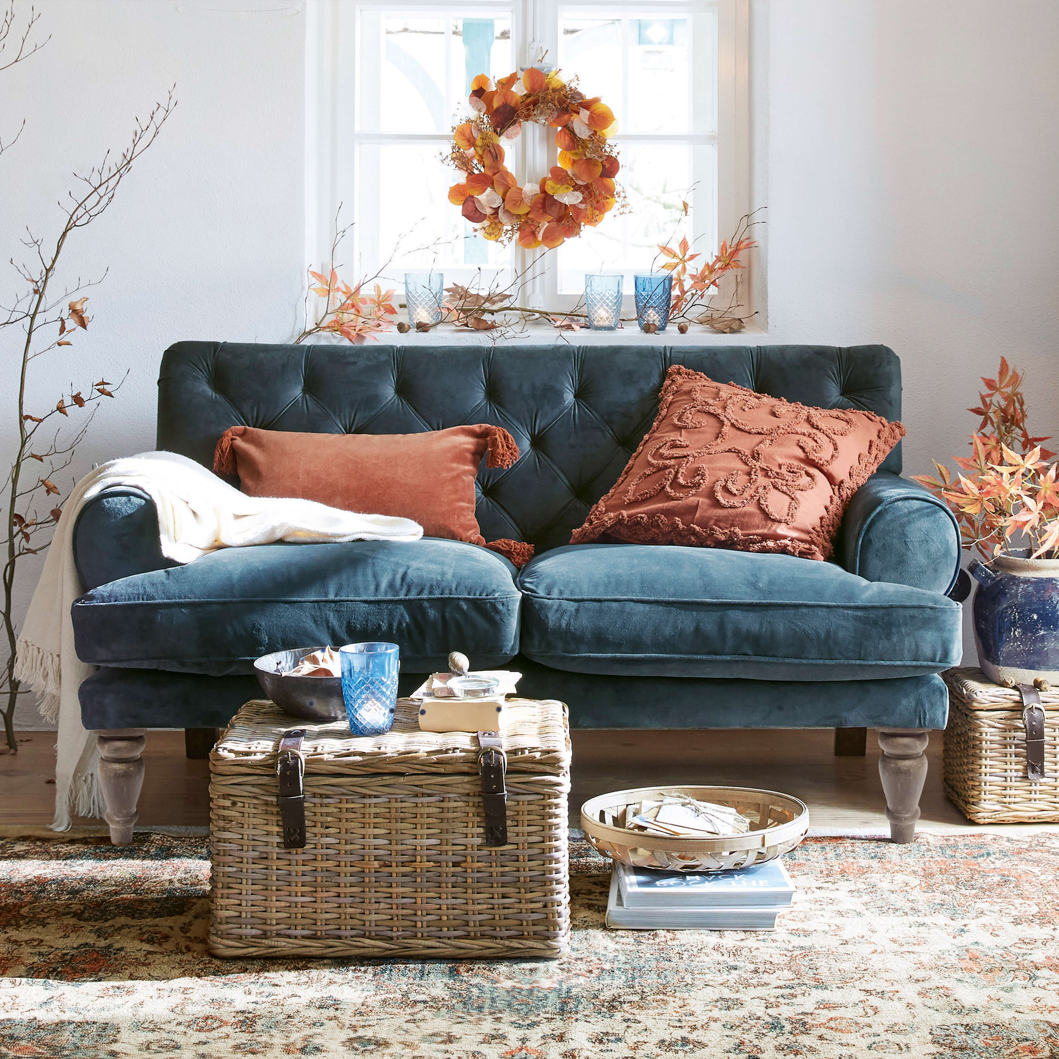 Sofá de terciopelo azul oscuro con cojines color óxido y mesa de mimbre en salón acogedor