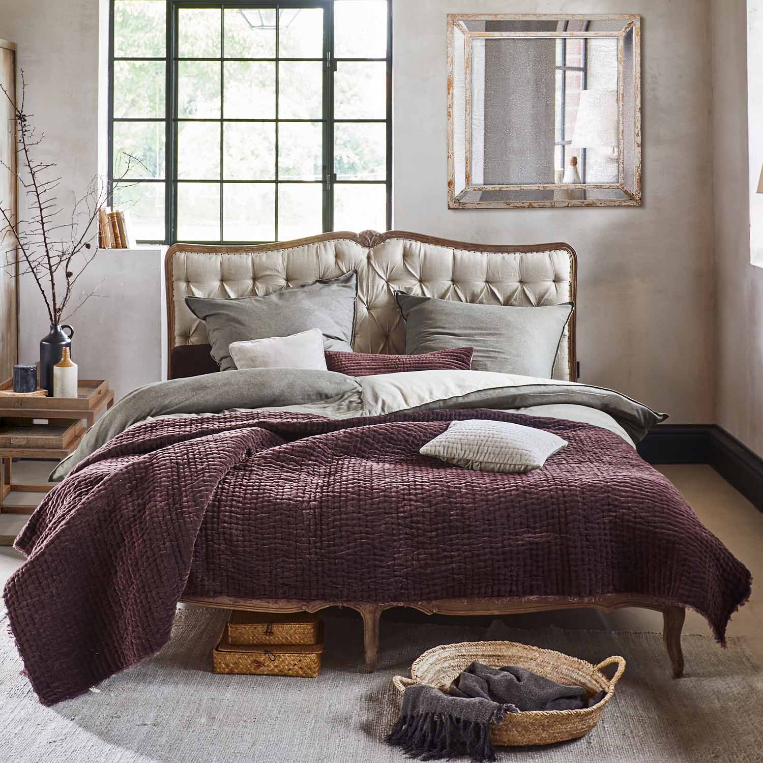 Cama con cabecero beige acolchado y colcha burdeos de material suave en estilo vintage
