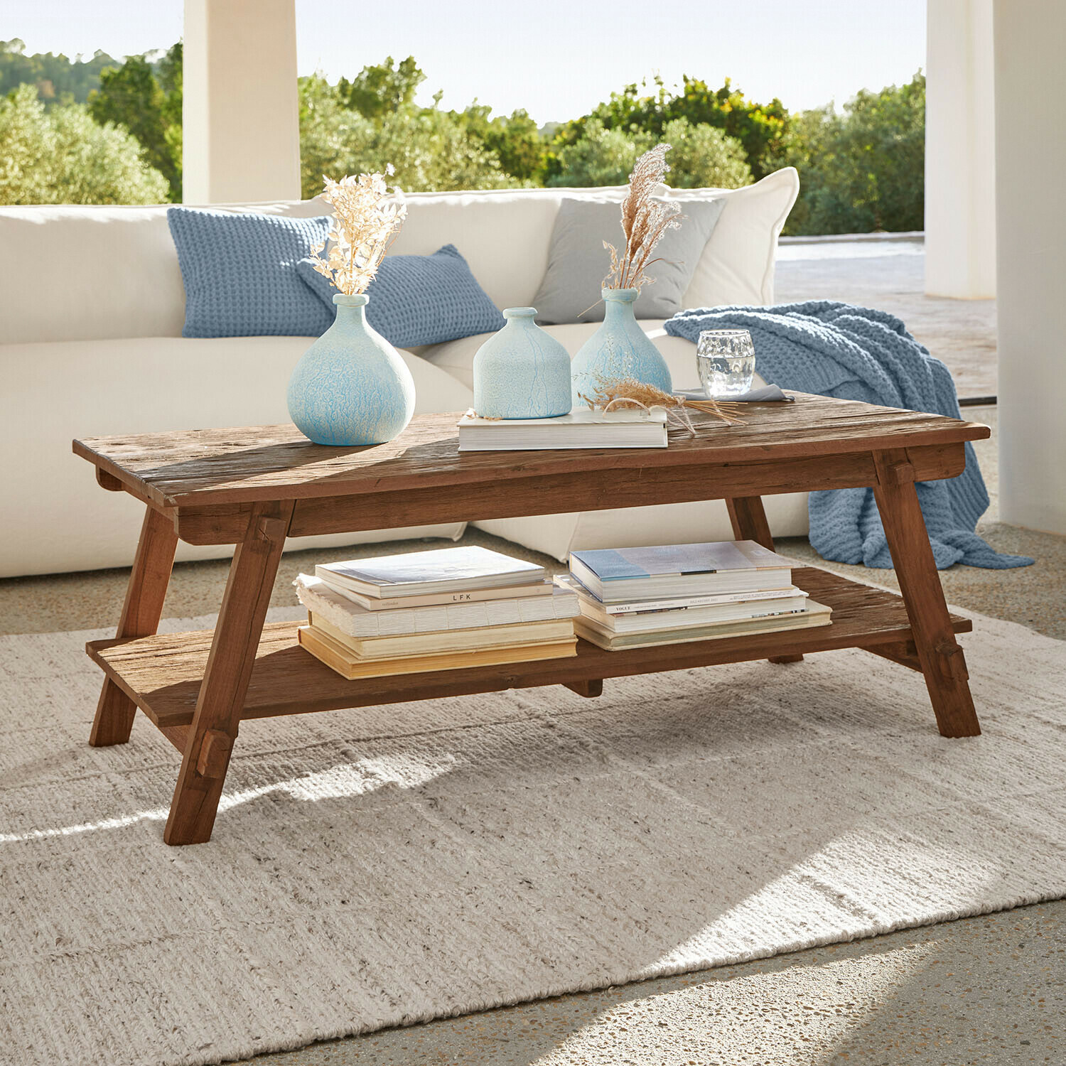 Mesa de centro de madera de mango en color natural con estante inferior, decorada con jarrones azules y libros