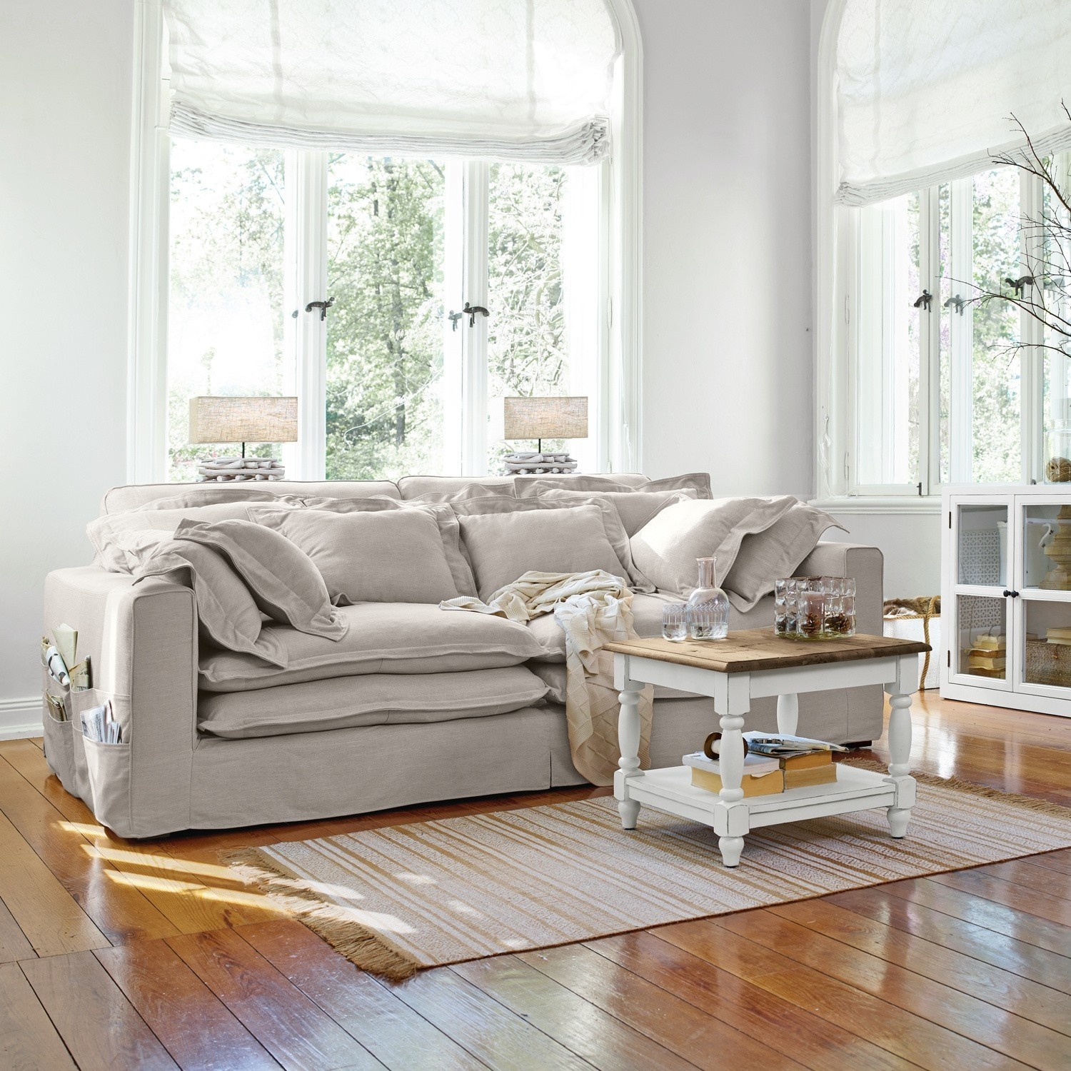 Sofá beige de tela con cojines y mesa de centro blanca sobre suelo de madera en salón luminoso