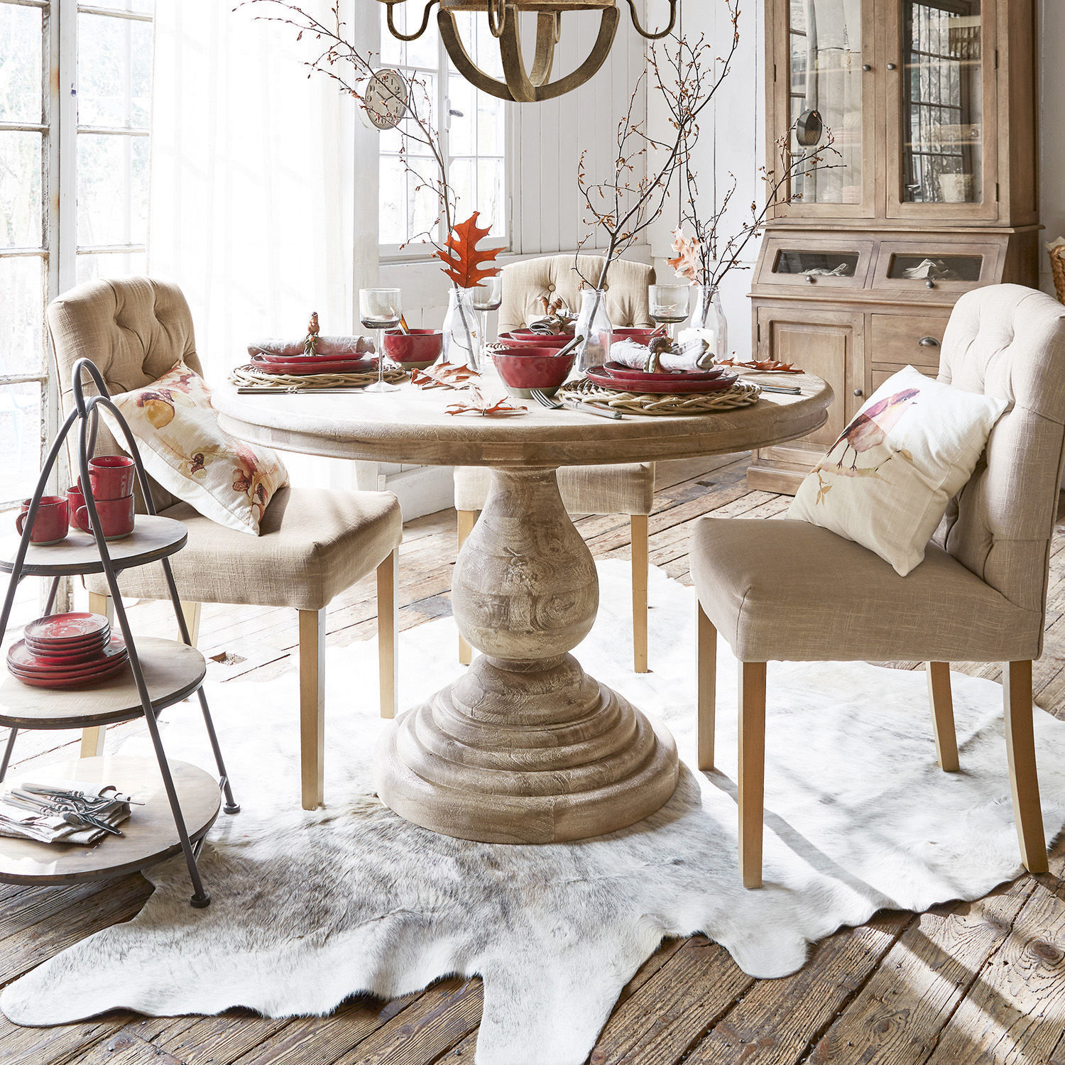 Mesa redonda de madera clara con sillas tapizadas beige y vajilla roja en comedor luminoso