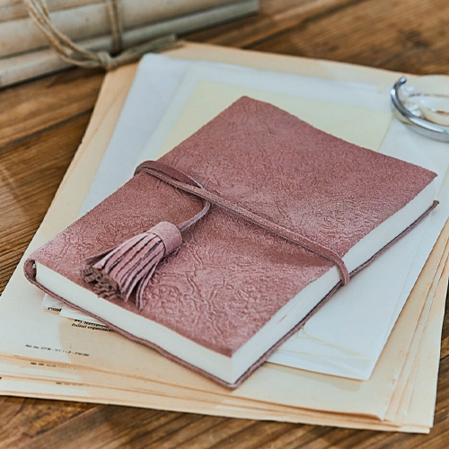 Cuaderno rosa de cuero suave con relieve y borla sobre documentos en mesa de madera