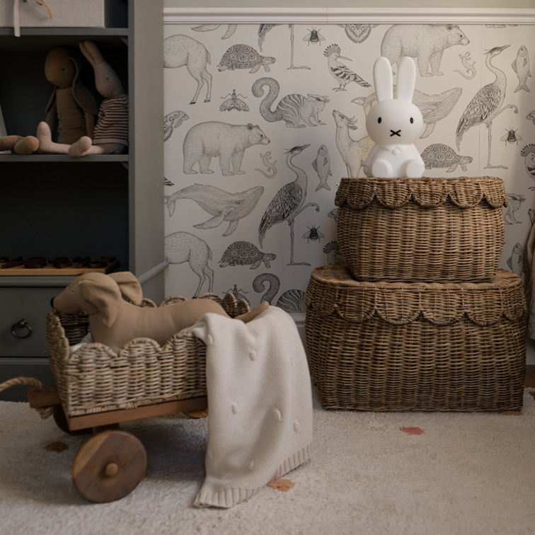 Dos cestas de mimbre marrón con lámpara de conejo y juguetes en habitación infantil con papel pintado de animales