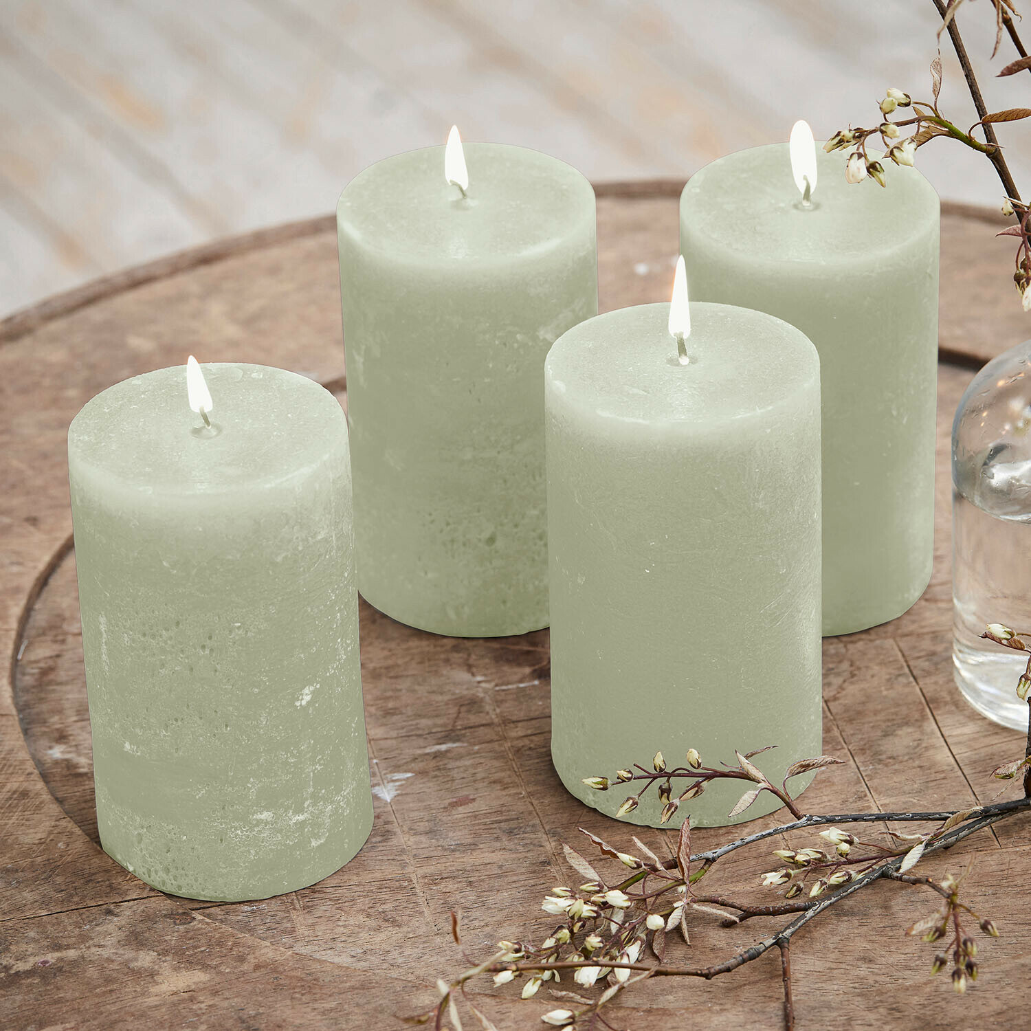 Set de 4 velas Braga Conjunto de cuatro velas verdes de cera sobre mesa de madera con decoración floral