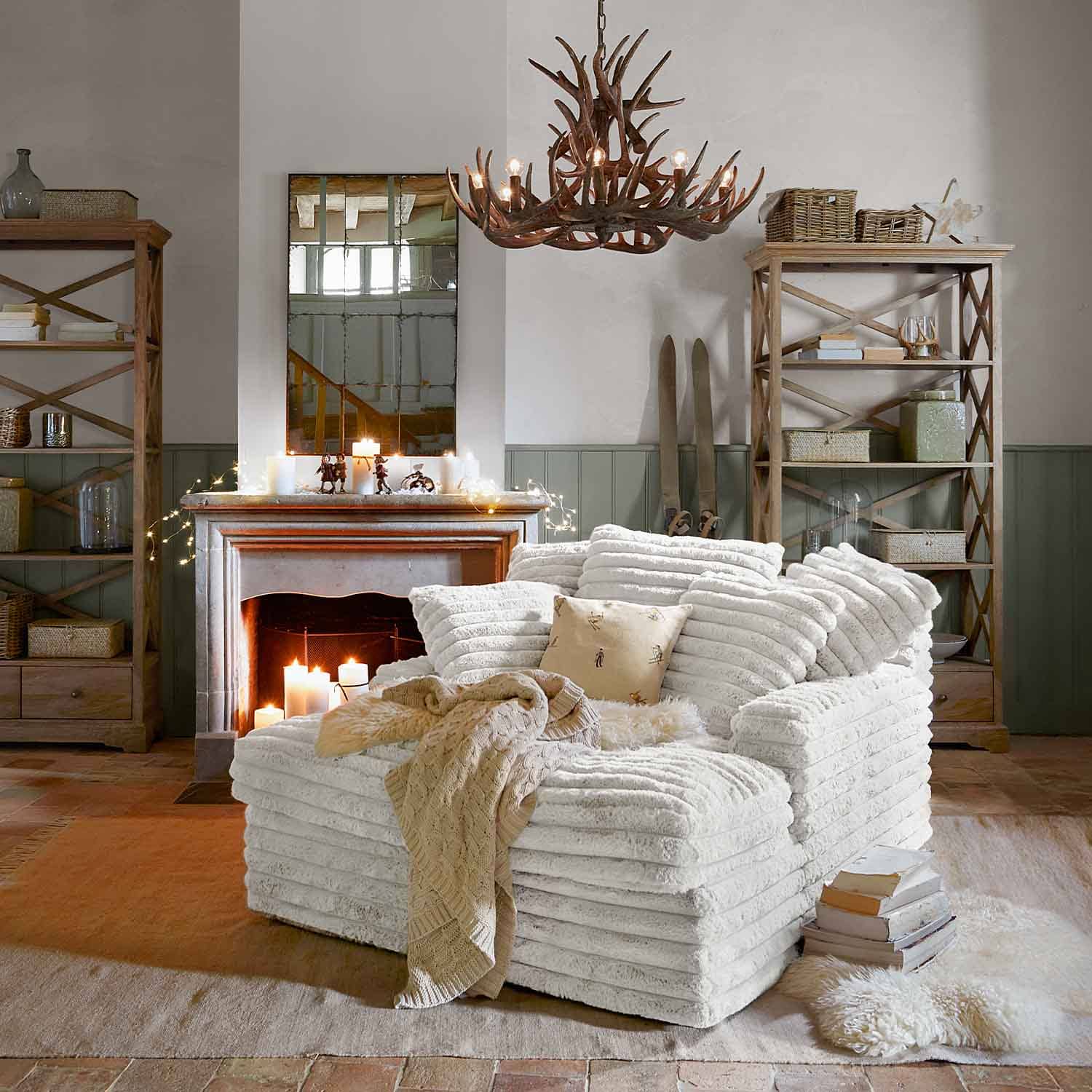 Sillón blanco acogedor de material suave en salón rústico con chimenea y estanterías de madera