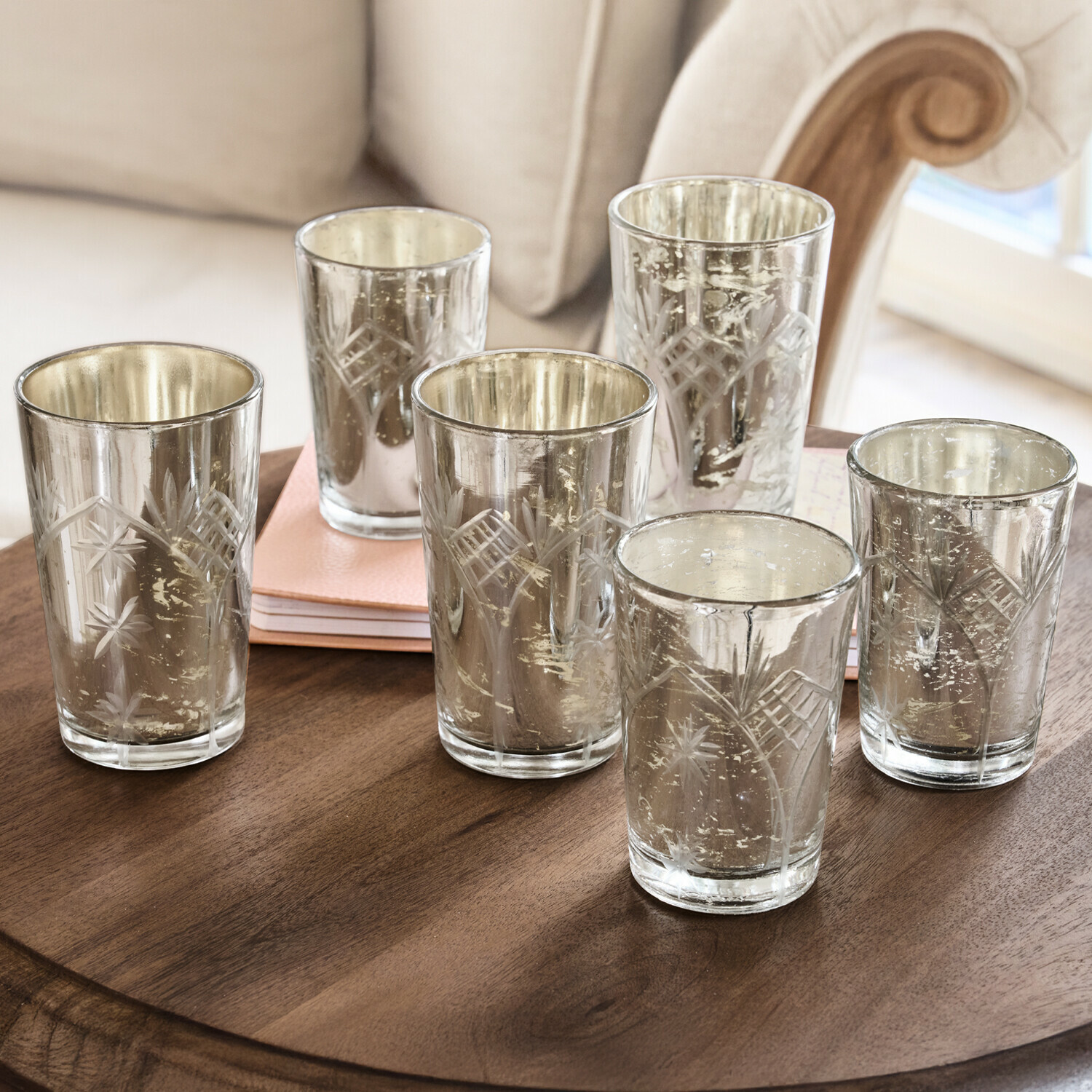 Conjunto de seis portavelas de vidrio grabado con acabado plateado sobre mesa de madera
