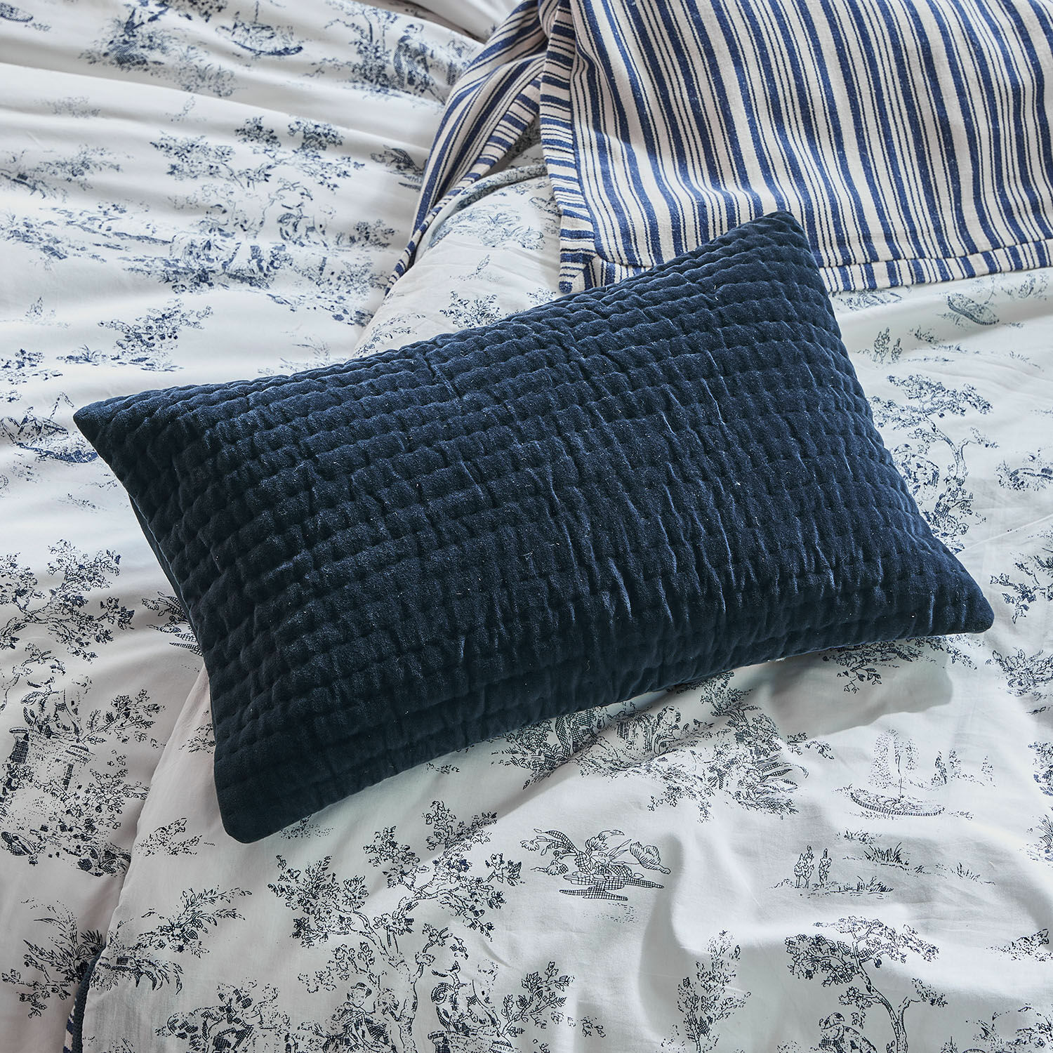 Funda de cojín Winklet Cojín acolchado azul marino sobre ropa de cama blanca con estampado azul, textil para dormitorio