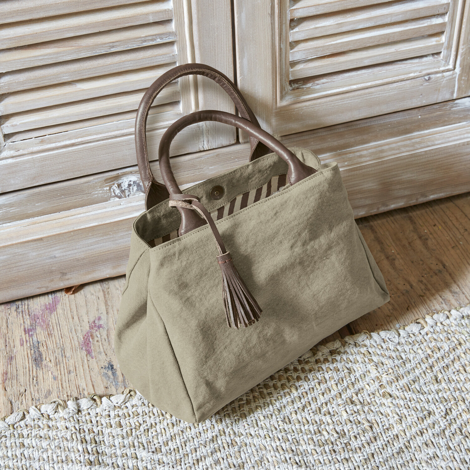 Bolso Hoya Bolso beige de tela con asas de cuero marrón y borla sobre suelo de madera