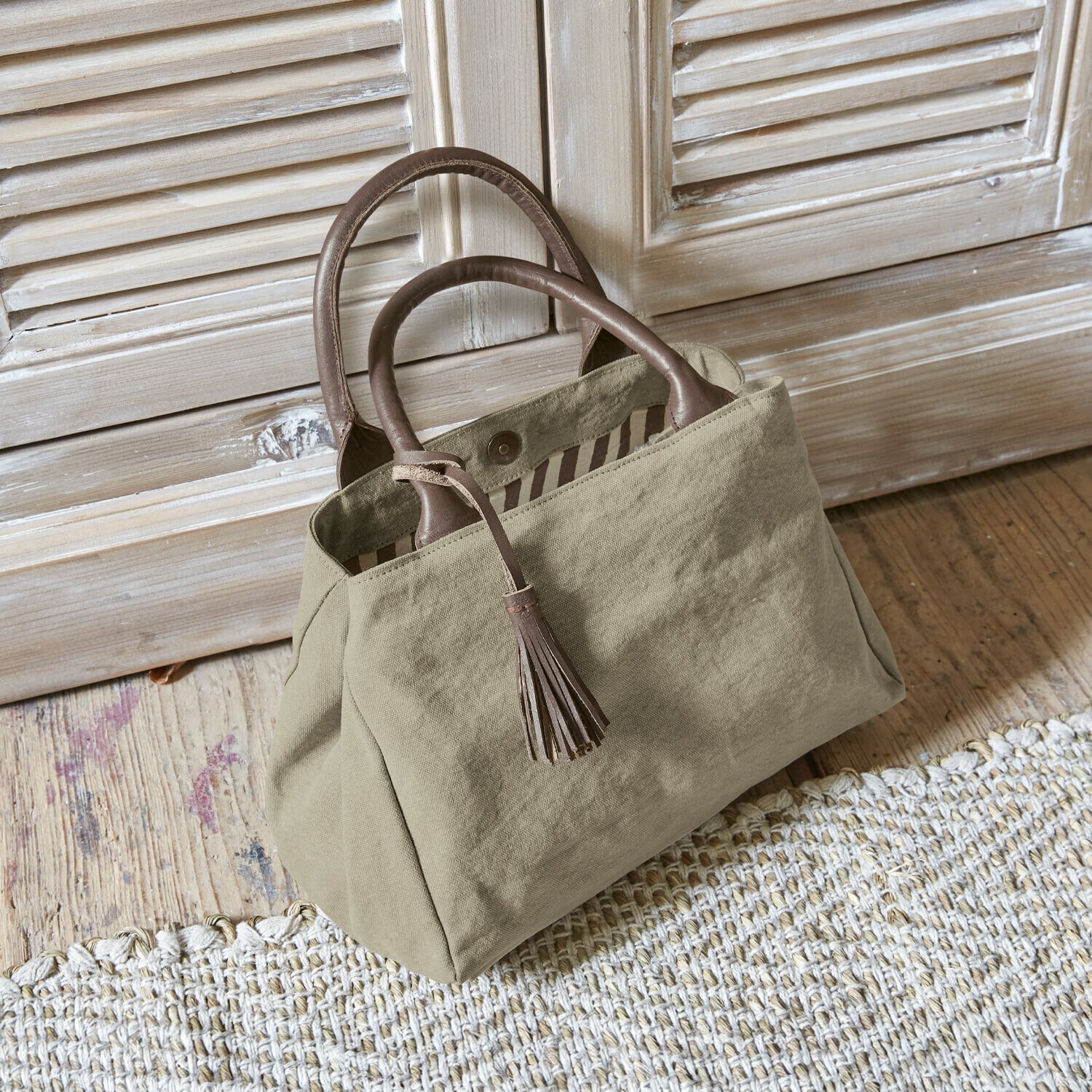 Bolso Hoya Bolso beige de tela con asas de cuero marrón y borla sobre suelo de madera