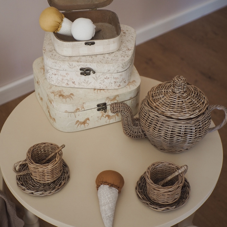 Juego de té infantil de mimbre con tetera y tazas sobre mesa redonda beige