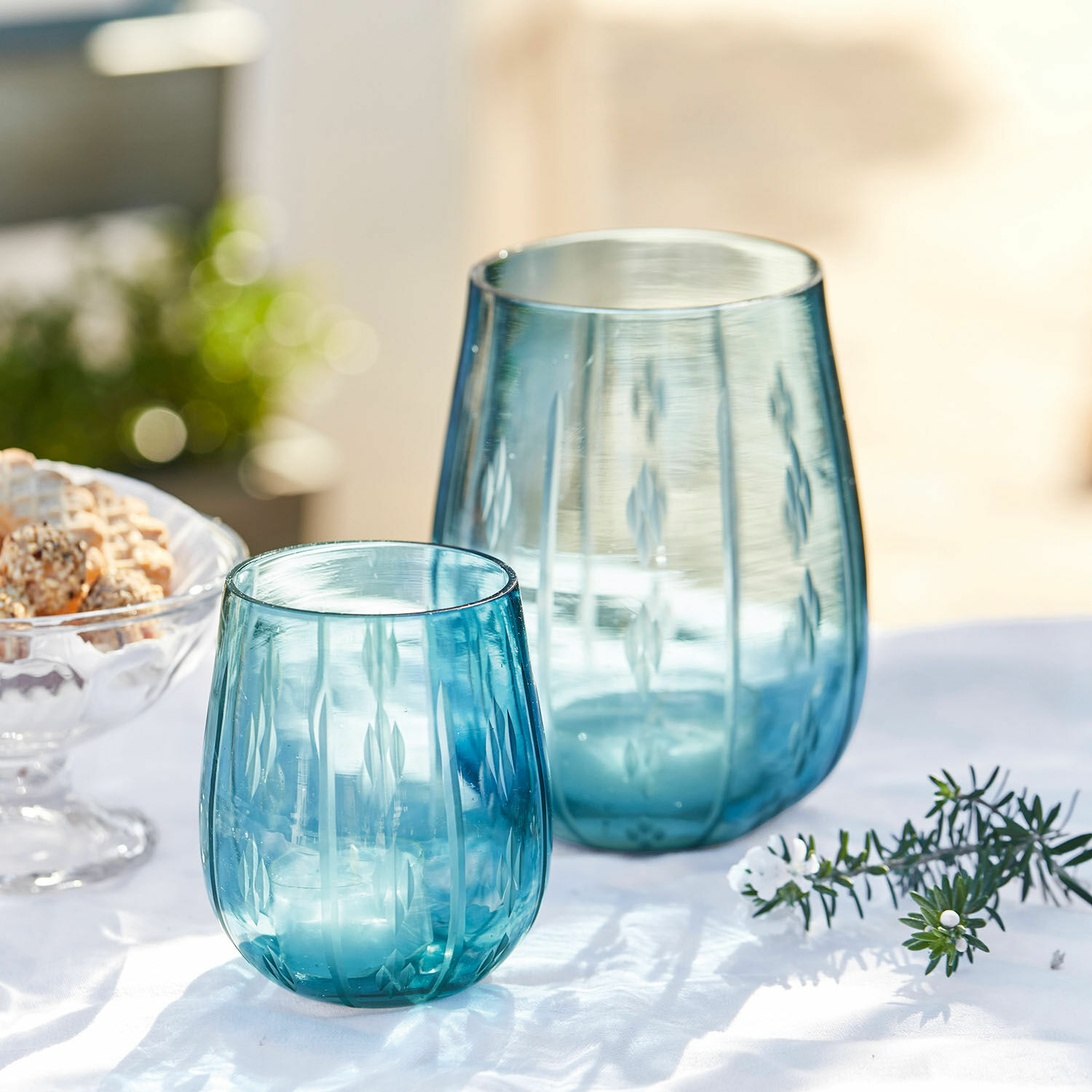 Set de 2 farolillos Danisar Dos portavelas de vidrio azul con diseño grabado sobre fondo blanco, decoración de mesa