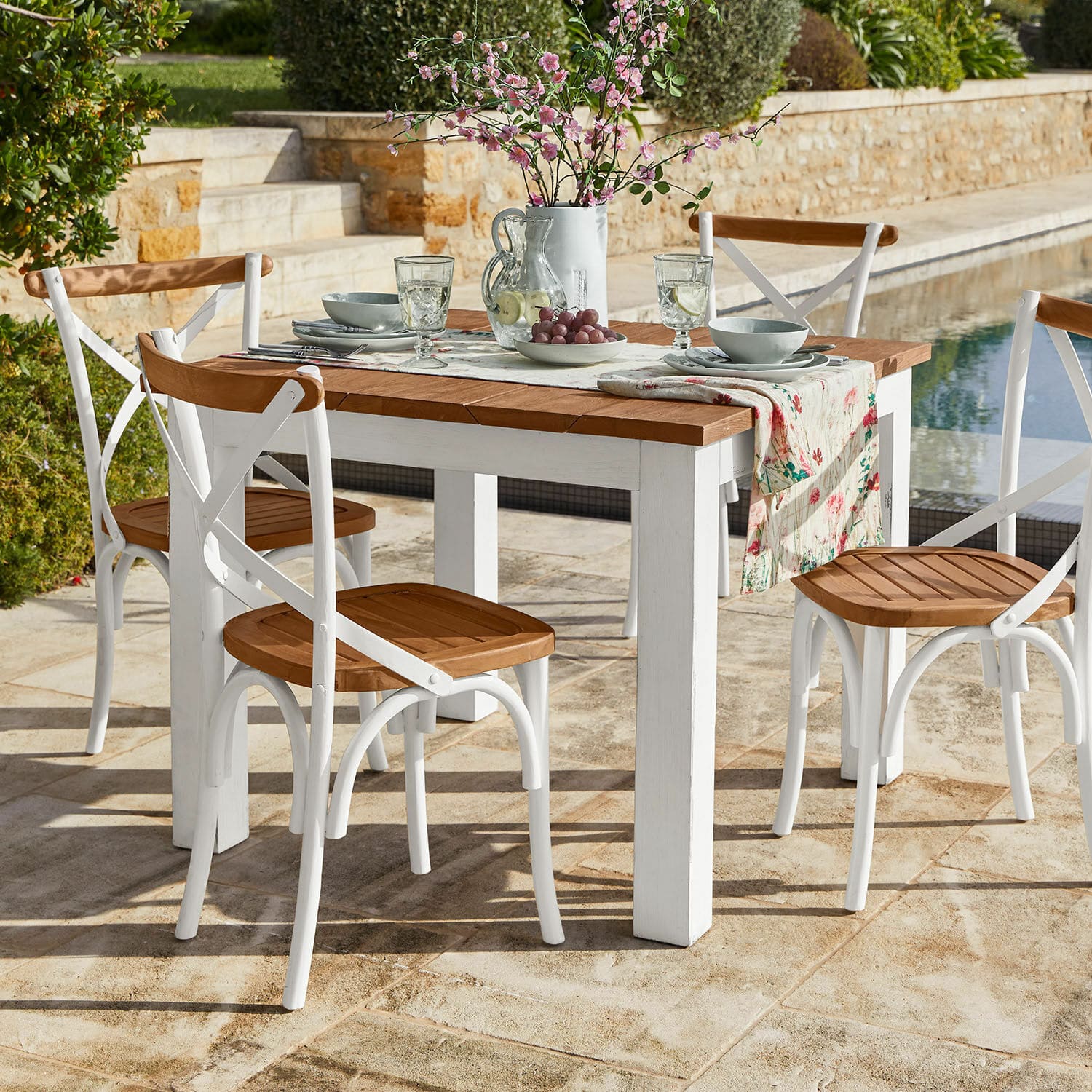 Mesa Kirkdale Conjunto de muebles de jardín con mesa blanca de madera y sillas con asiento de madera en terraza de piedra