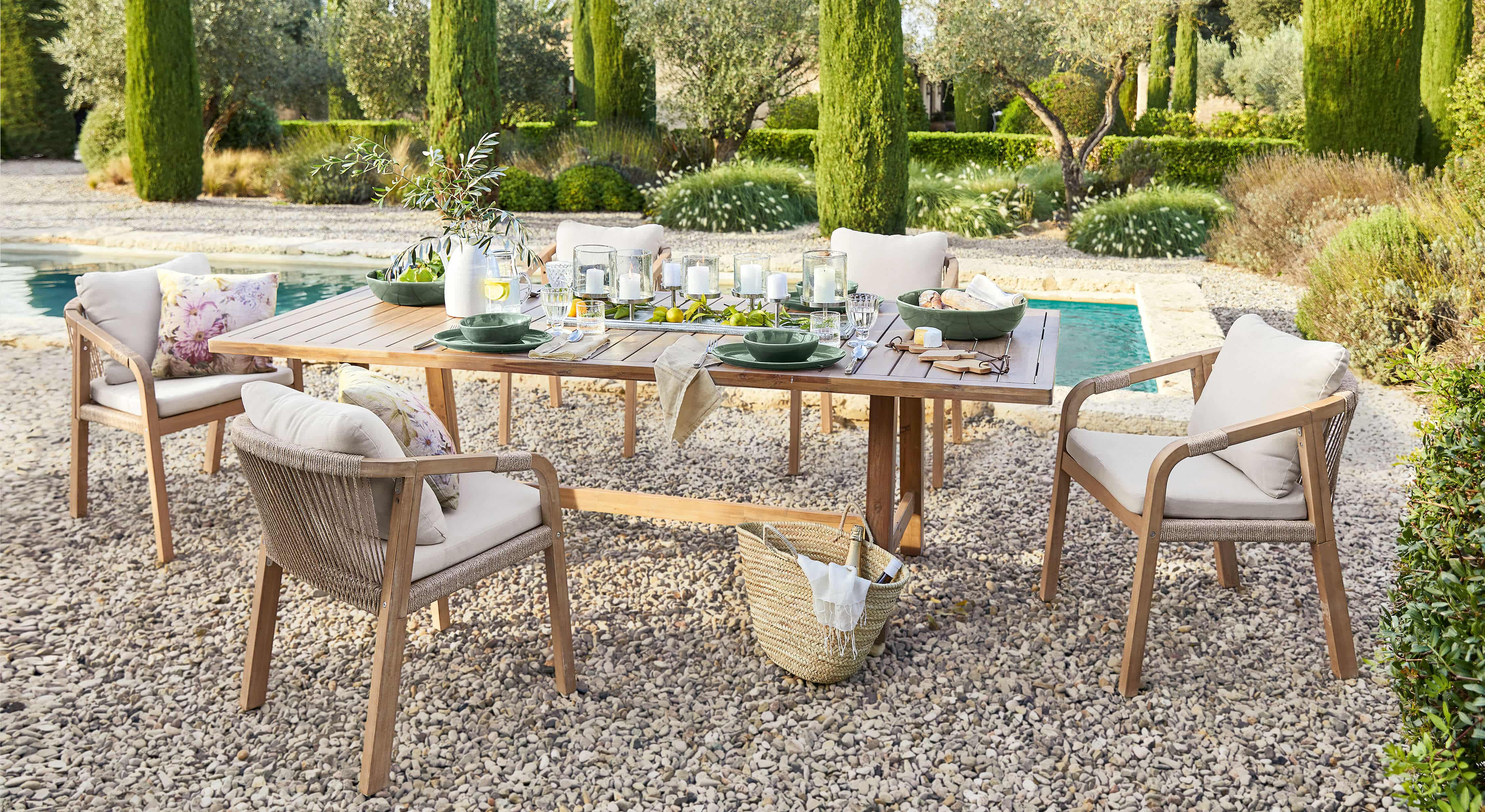 Conjunto de muebles de jardín con mesa de madera y sillas beige en patio de grava junto a piscina