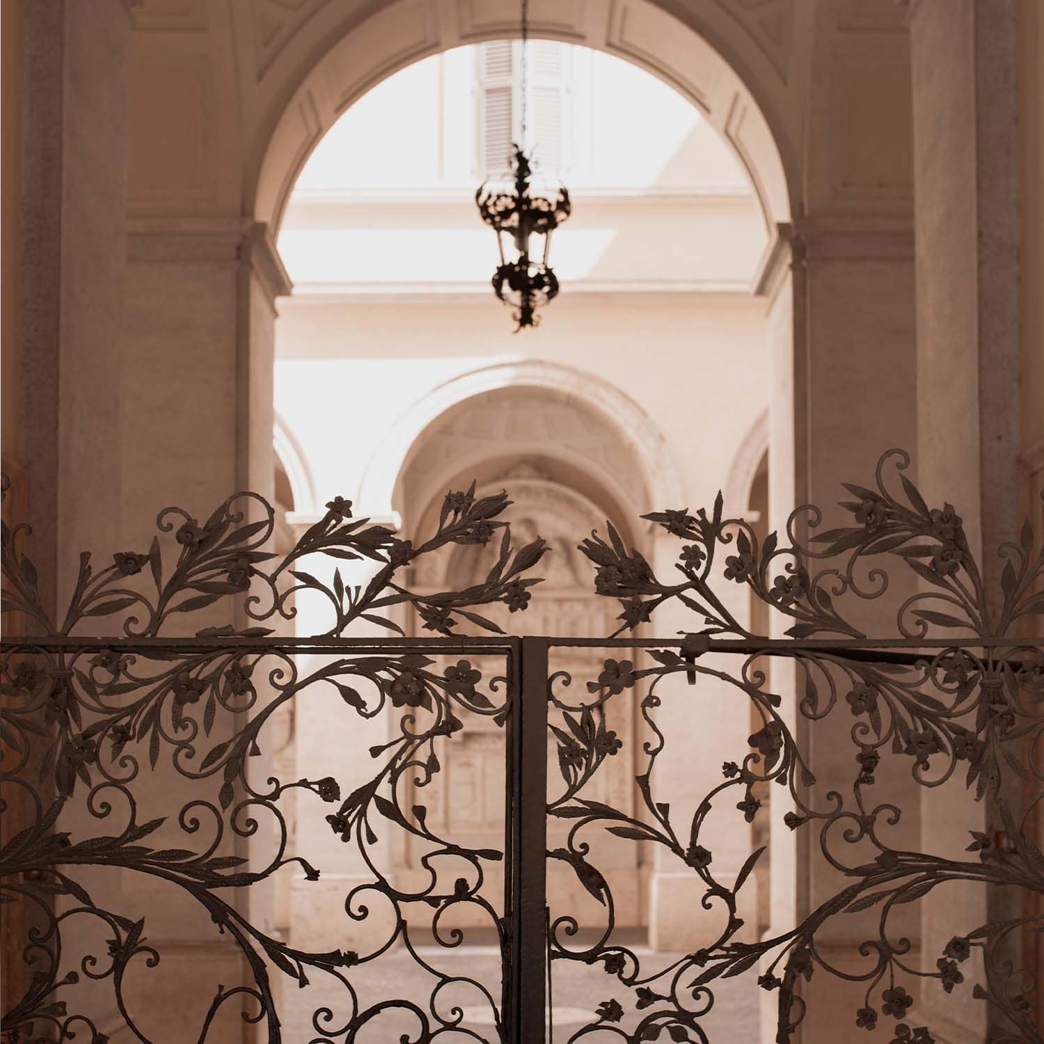 Puerta de hierro forjado con motivos florales frente a un interior luminoso con arcos claros