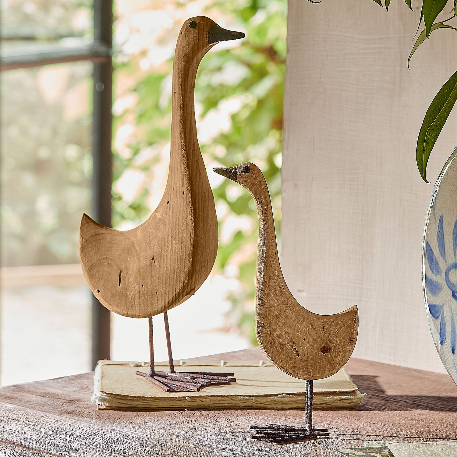Decoraciones de madera en forma de pájaros con patas de metal sobre mesa, color madera natural