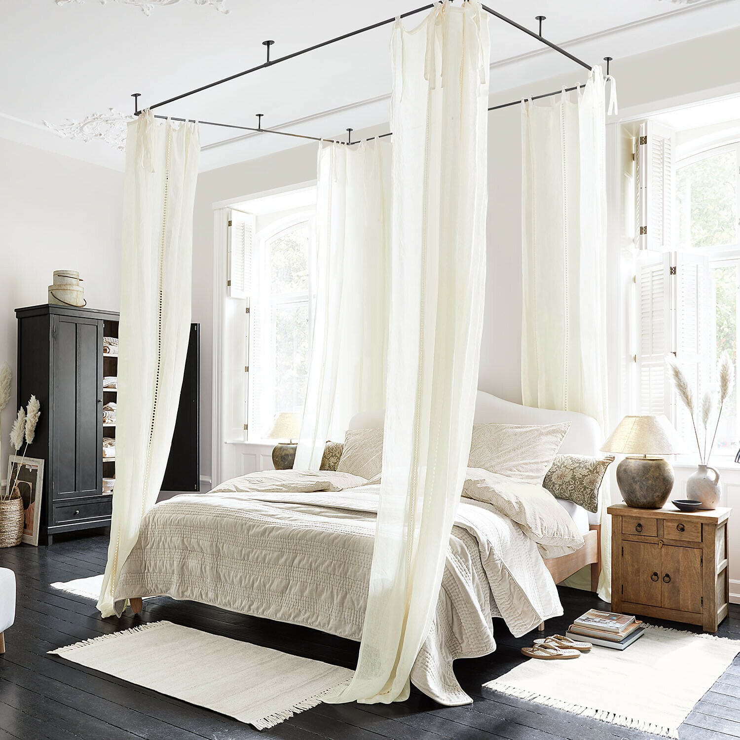 Cortina Elorine Dormitorio con cama con dosel de algodón blanco y ropa de cama beige sobre suelo de madera oscura, luz natural