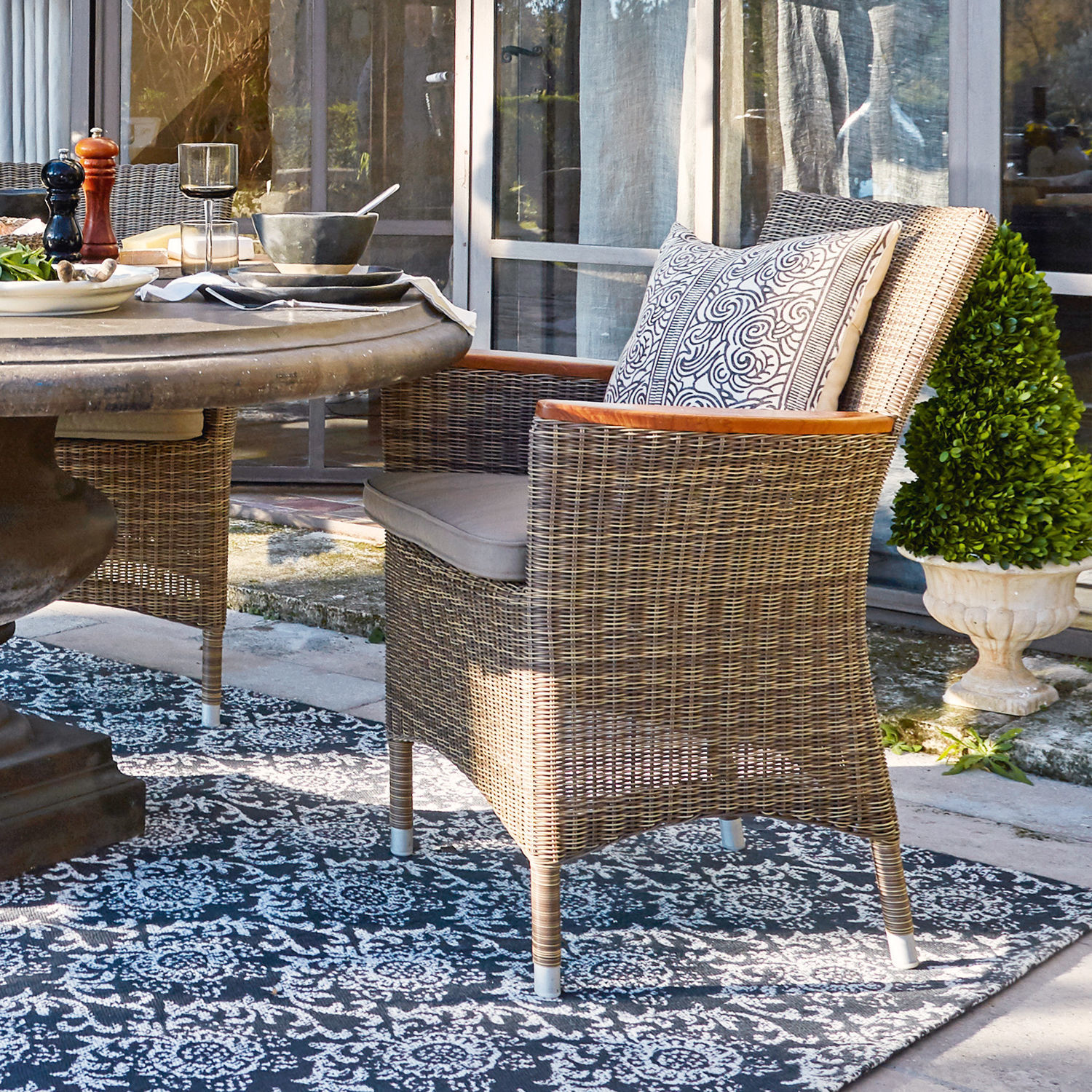 Silla de ratán color natural con cojín y reposabrazos de madera en terraza exterior