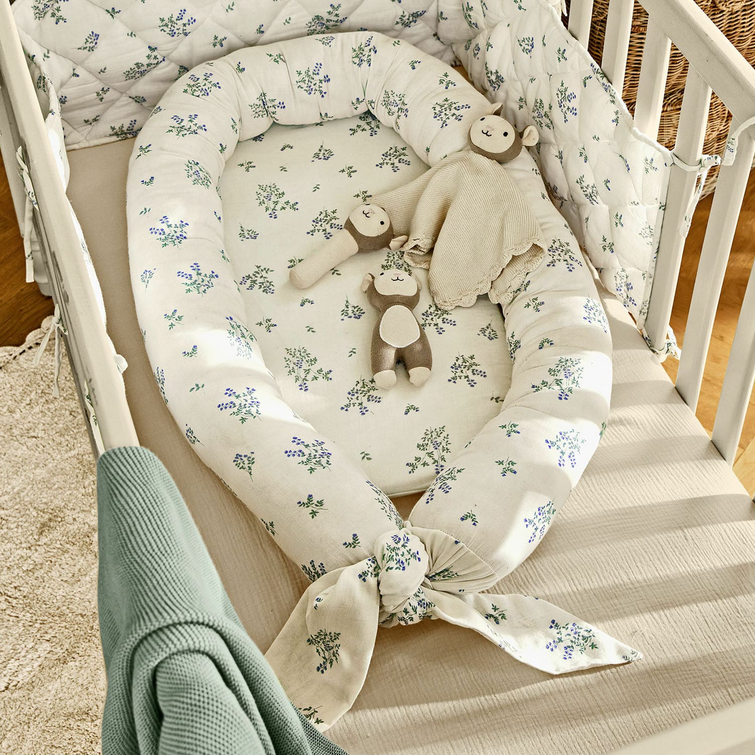 Nido de bebé Nymariel Nido para bebé blanco de algodón con estampado floral azul-verde y peluches en cuna de madera clara