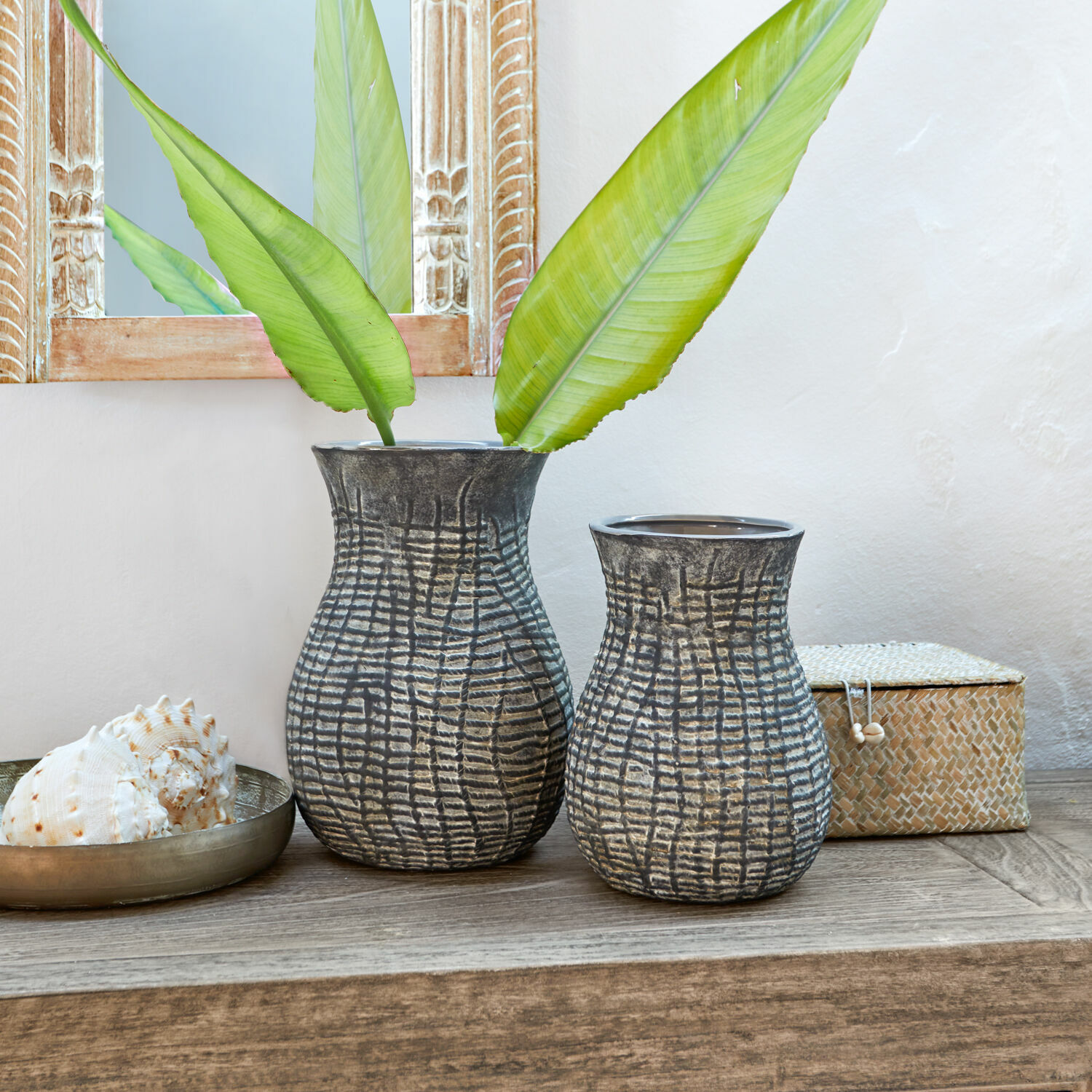 Set de 2 jarrones Fahrid Dos jarrones de cerámica gris con patrón texturizado sobre mesa de madera con hojas verdes
