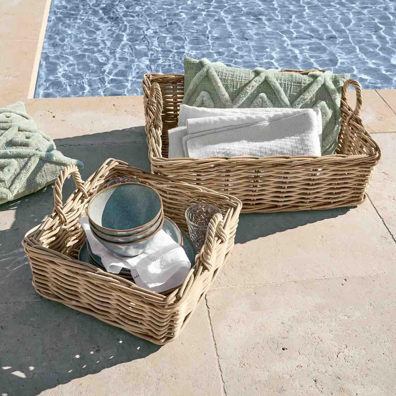 Dos cestas de mimbre con asas, con cojines verdes y toallas blancas, junto a la piscina